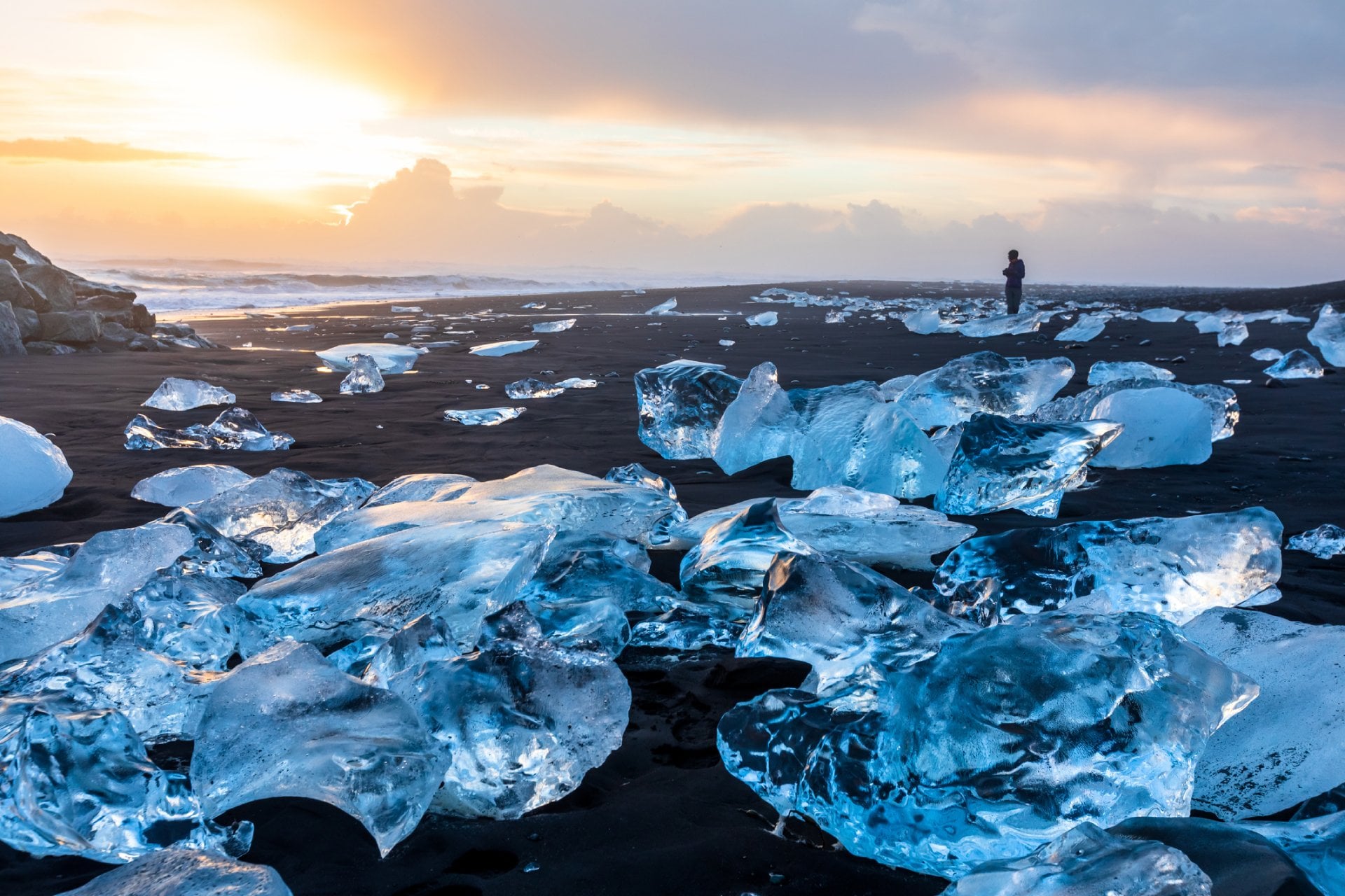 Diamond Beach in Iceland with blue icebergs melting on the black sand and ice glistening with sunrise sun light
