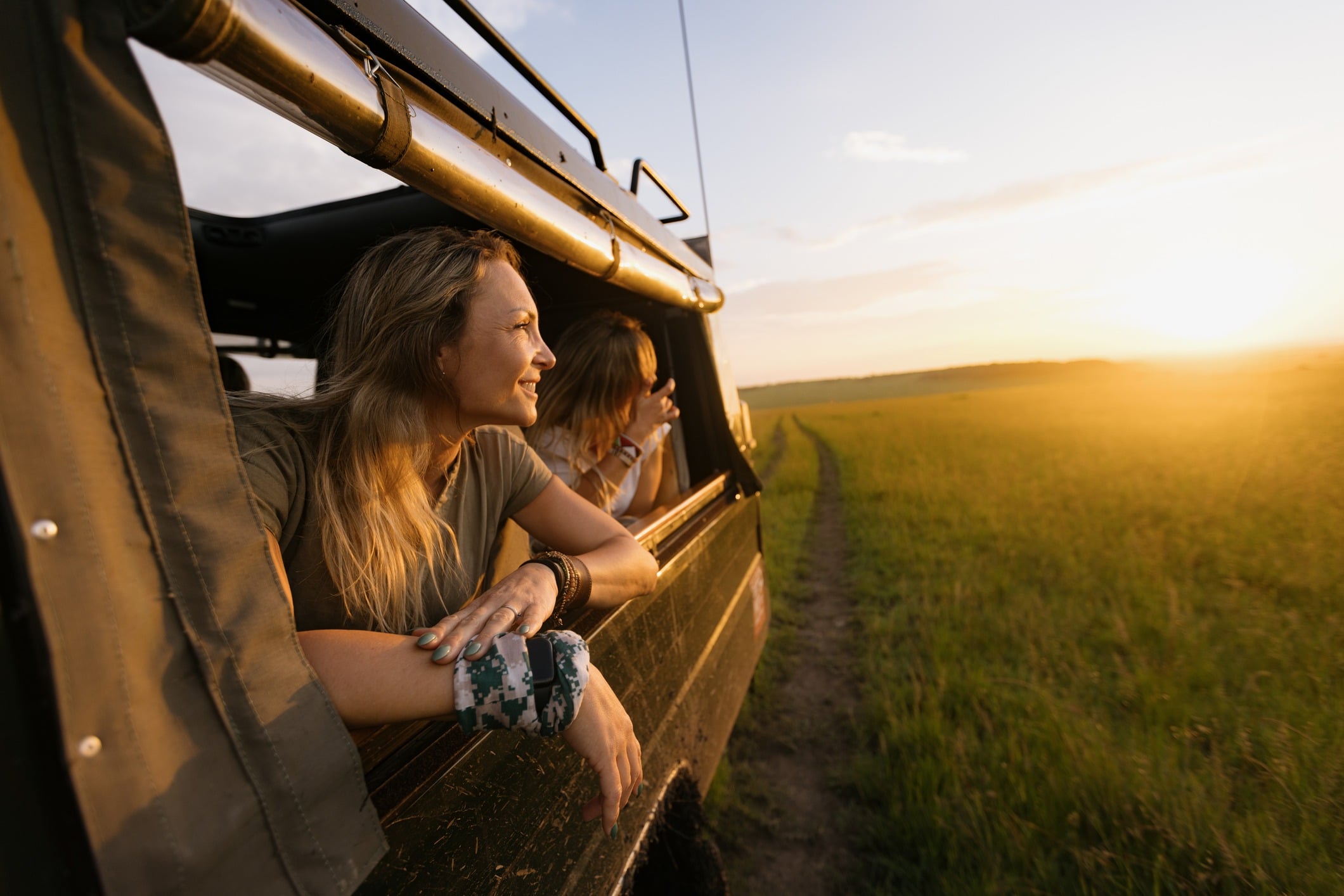 Kenya A woman in a Land Cruiser on a safari game drive at sunset leaning out of the vehicle window.