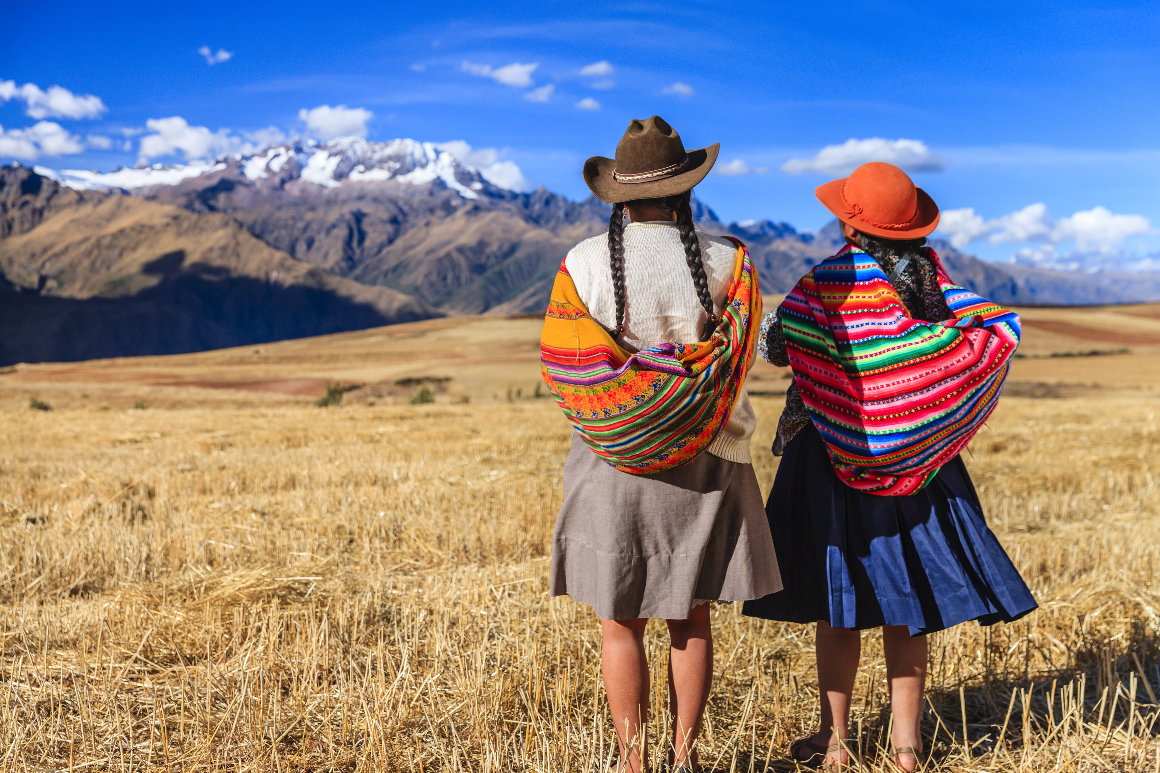 Two women walking across a grassy plain against a backdrop of mountains in Peru's Sacred Valley.