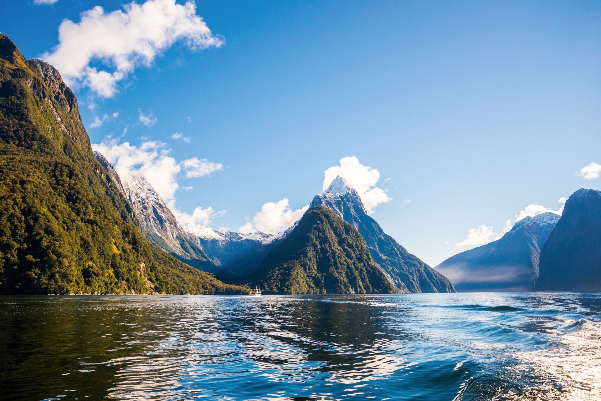 Milford Sound, New Zealand Towering forested peaks, snowy mountains, and calm blue waters under a clear sky in New Zealand’s dramatic Milford Sound fjord.