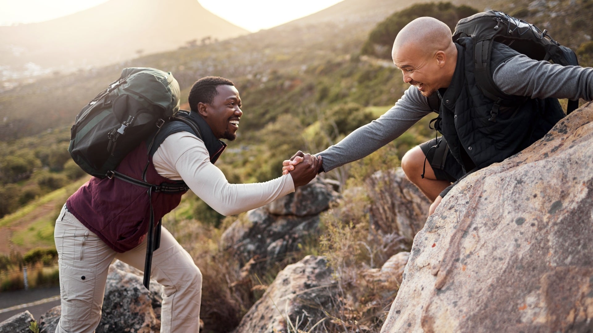 two hikers help each other get over rocks on a mountain