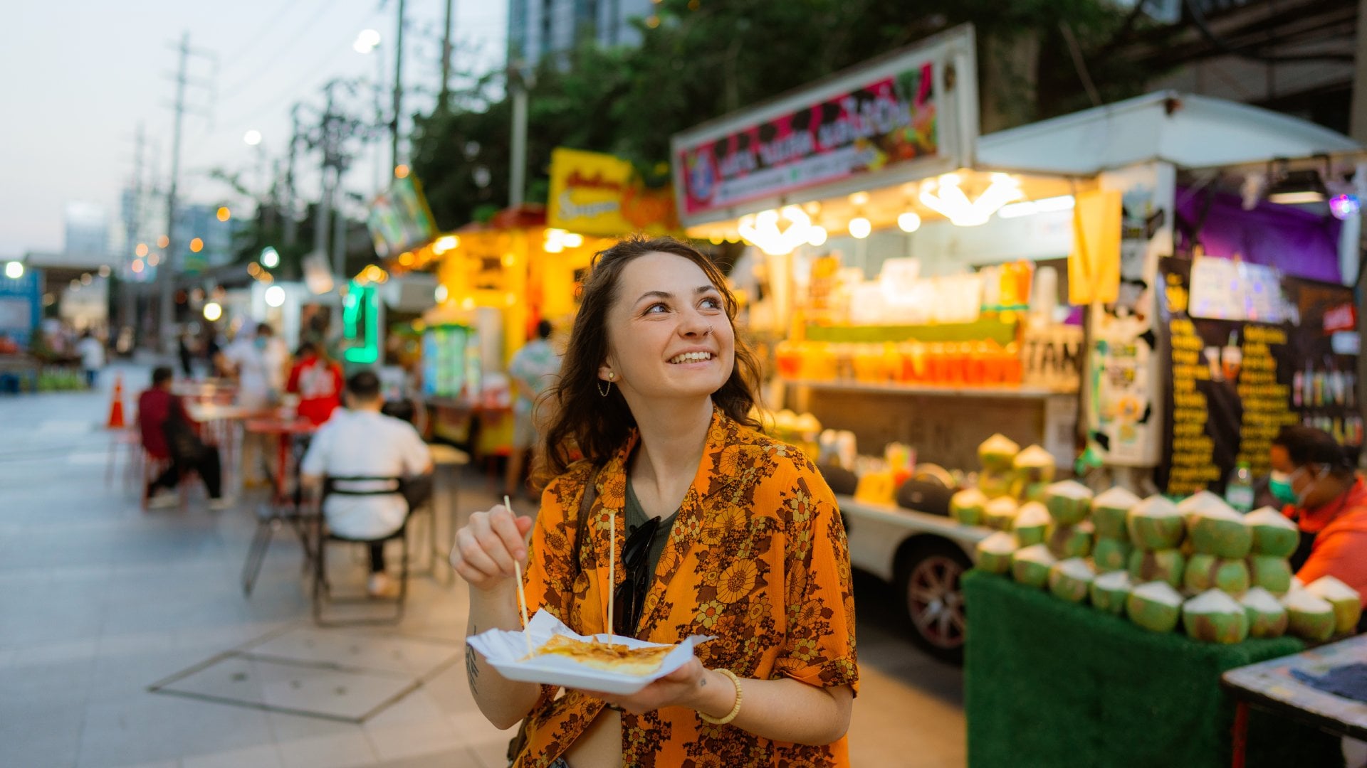 Cheerful woman eating thai pancakes (roti) on night market in Bangkok
