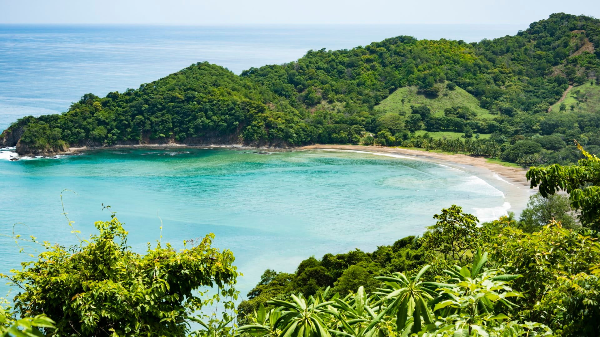 View of a small crescent beach hidden away among green hills and forests