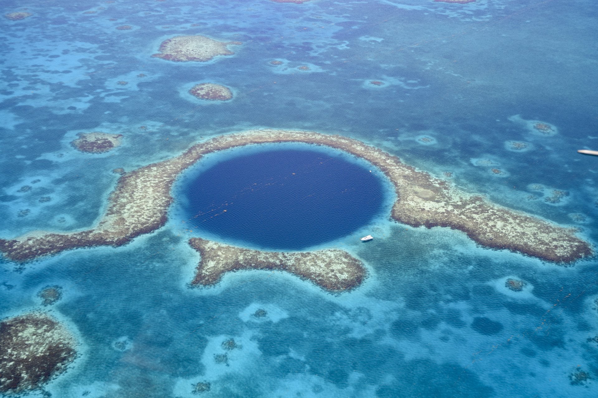 Aerial view of Great Blue Hole a marine sinkhole and geological wonder in the Belize Barrier Reef Reserve. A small white yacht is moored at it's edge