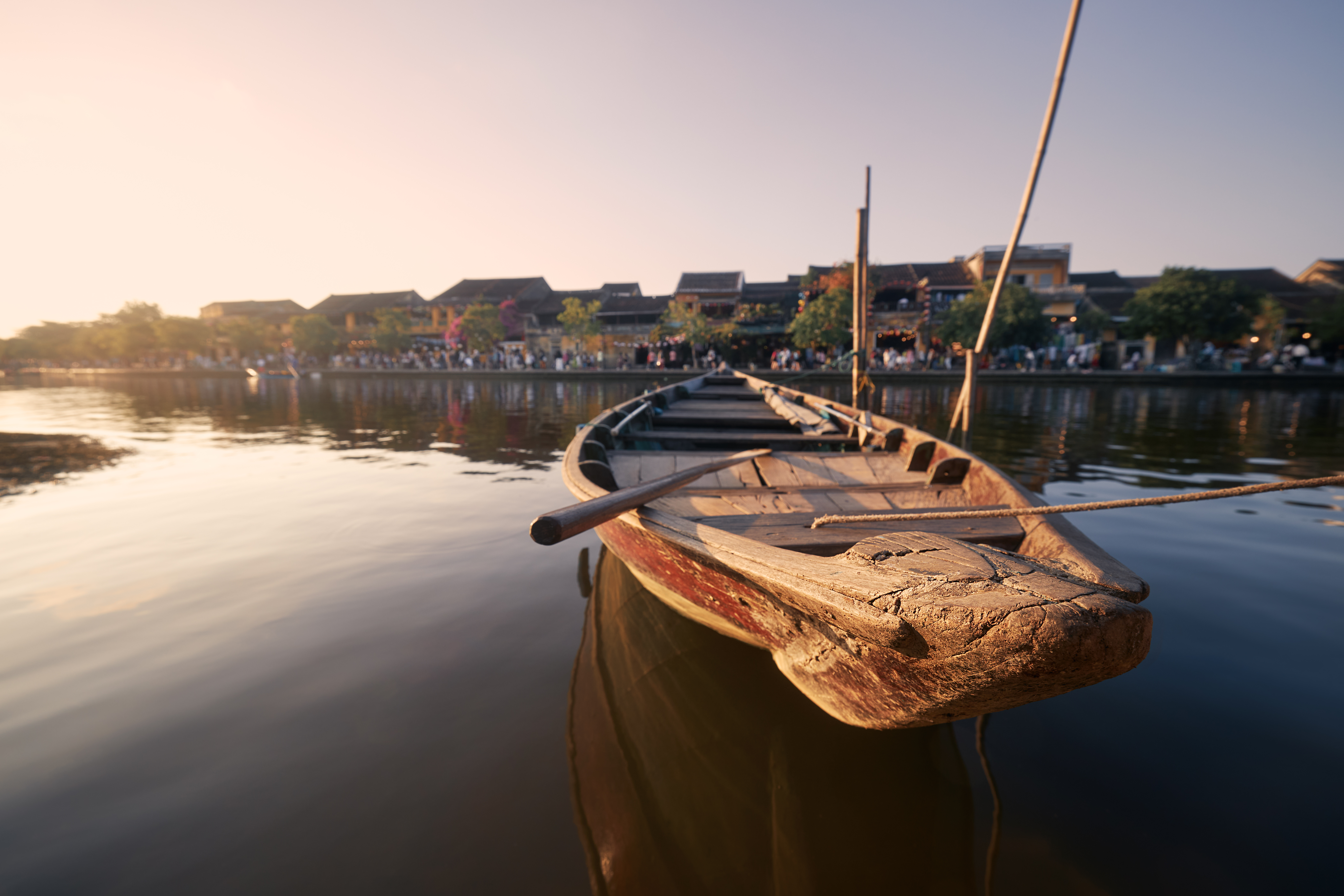 Close-up wooden boat moored against busy waterfront ancient city Hoi An at sunset.