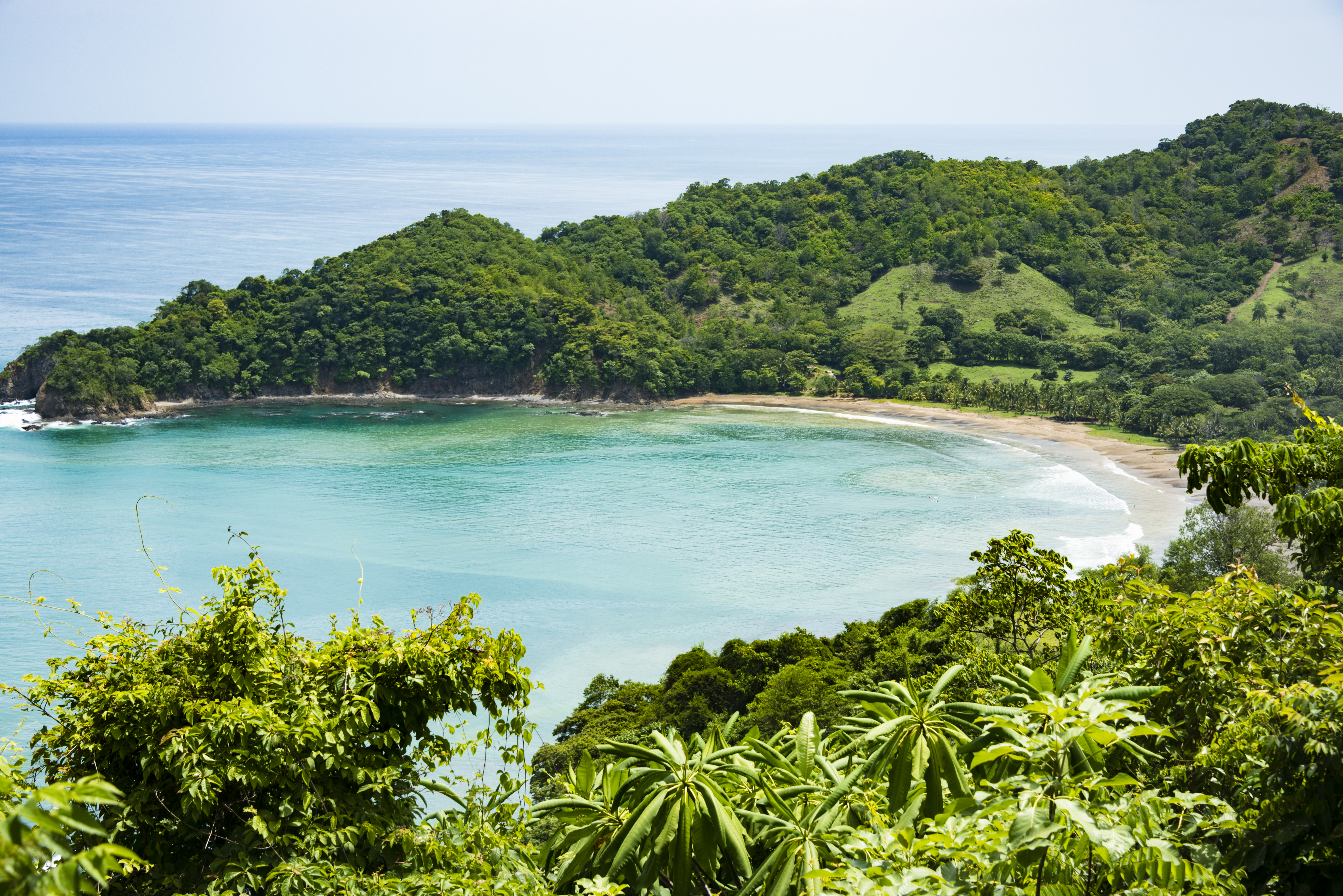 View of a small crescent beach hidden away among green hills and forests