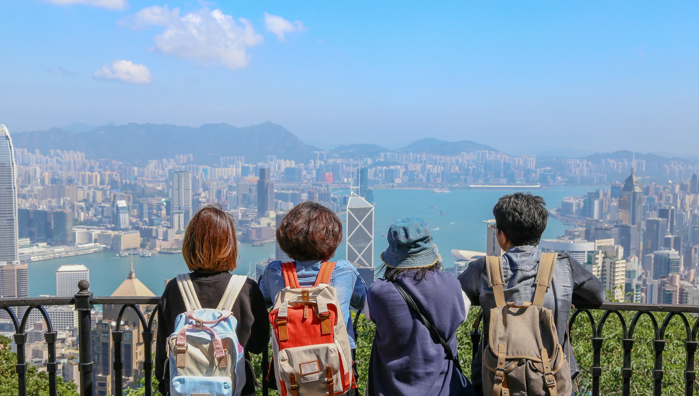 A group of four people look out over the Hong Kong skyline from a viewpoint on the mountain.