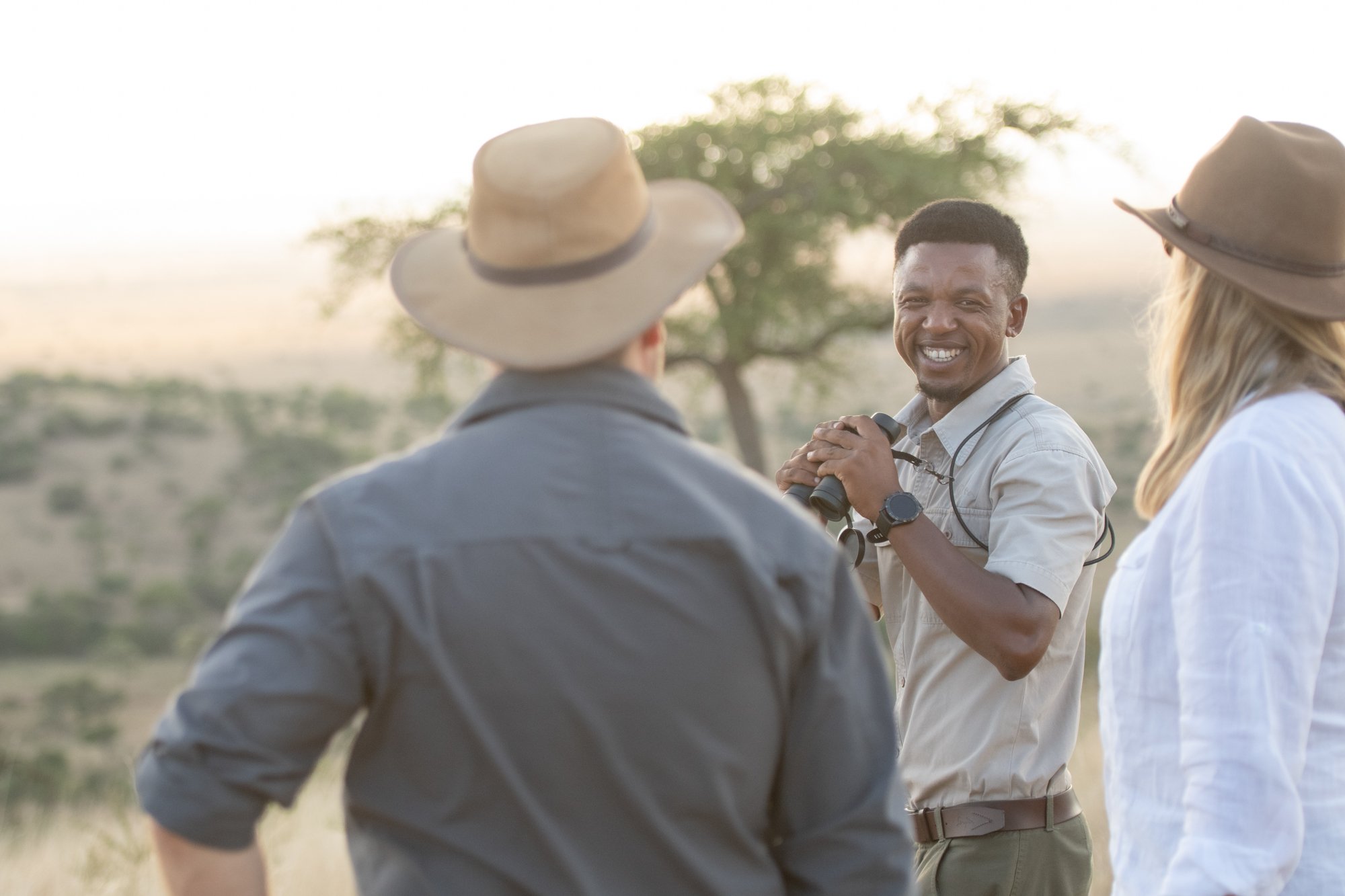 A guide holding binoculars talking to two guests at Singita in Grumeti Game Reserve in Tanzania