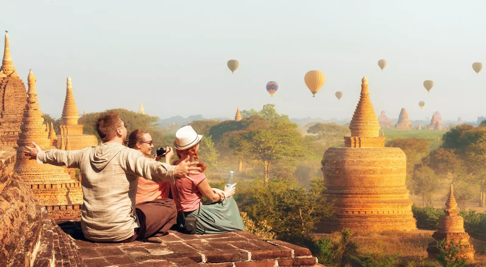 People sitting on the edge of a temple watching hot air balloons over Bagan, Myanmar