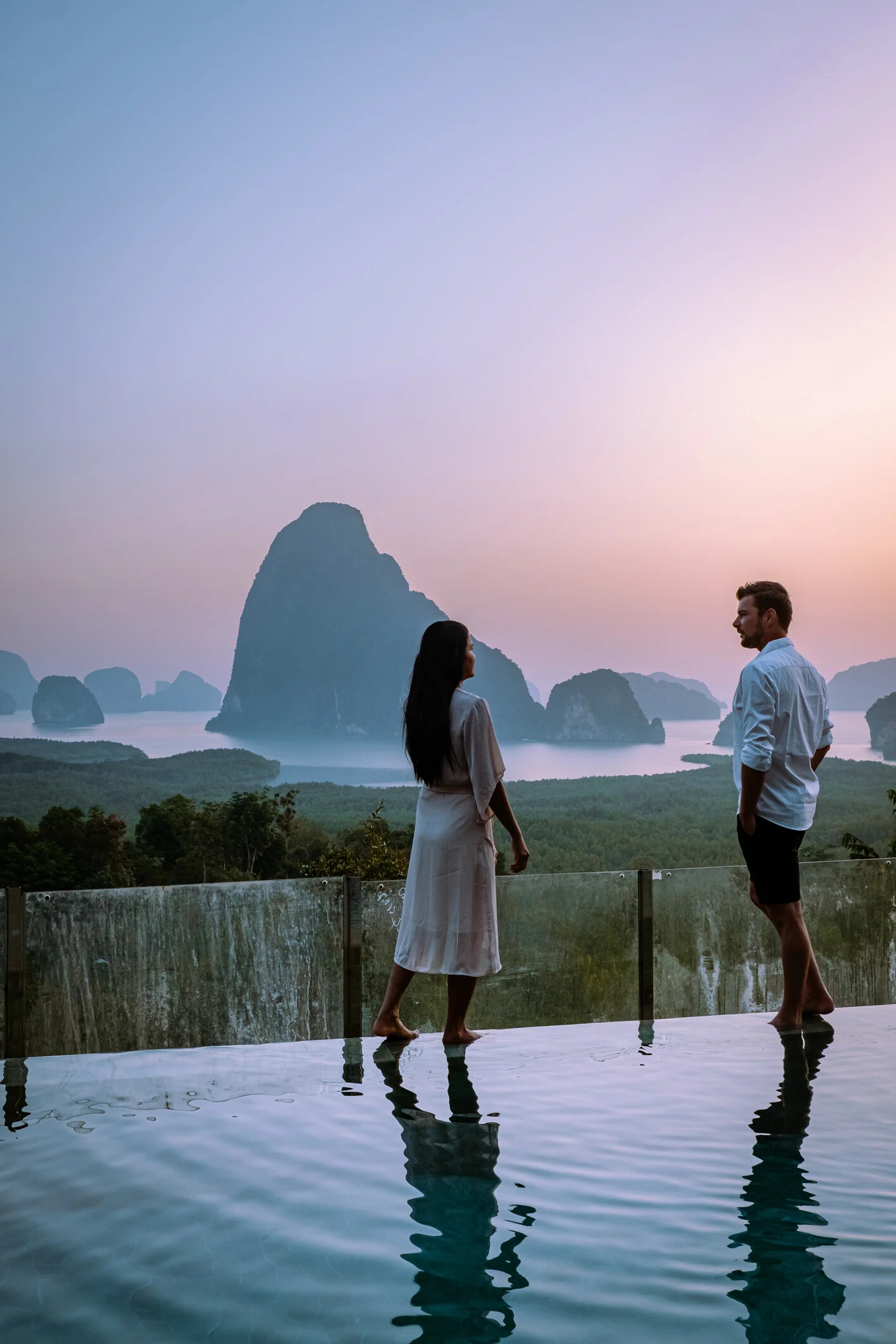 A couple walks along an infinity pool at dusk in Phang Nga Bay in Thailand.