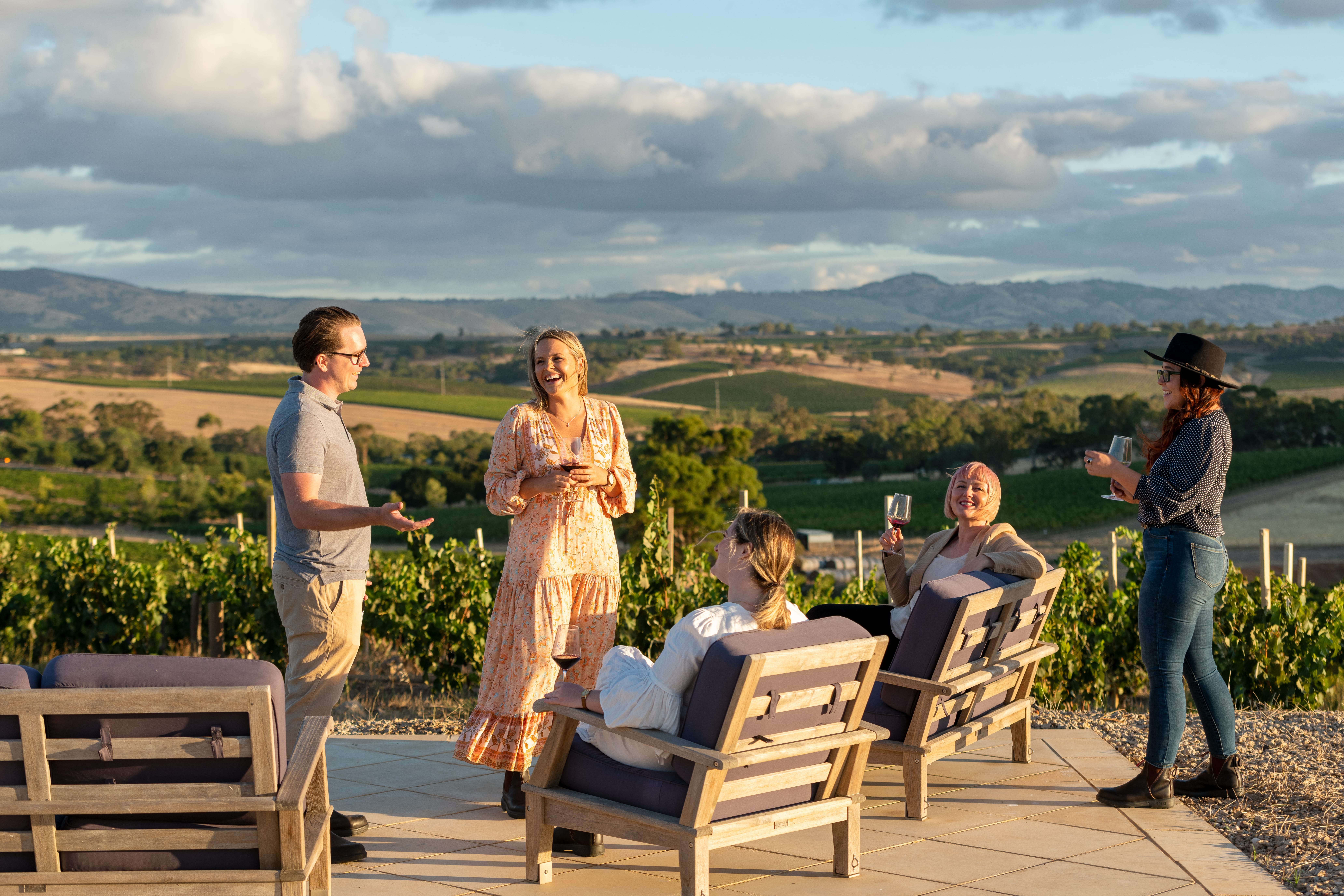 A group of five friends are smiling and lauging during an outdoor conversation at susnet in Barossa Valley, South Australia.