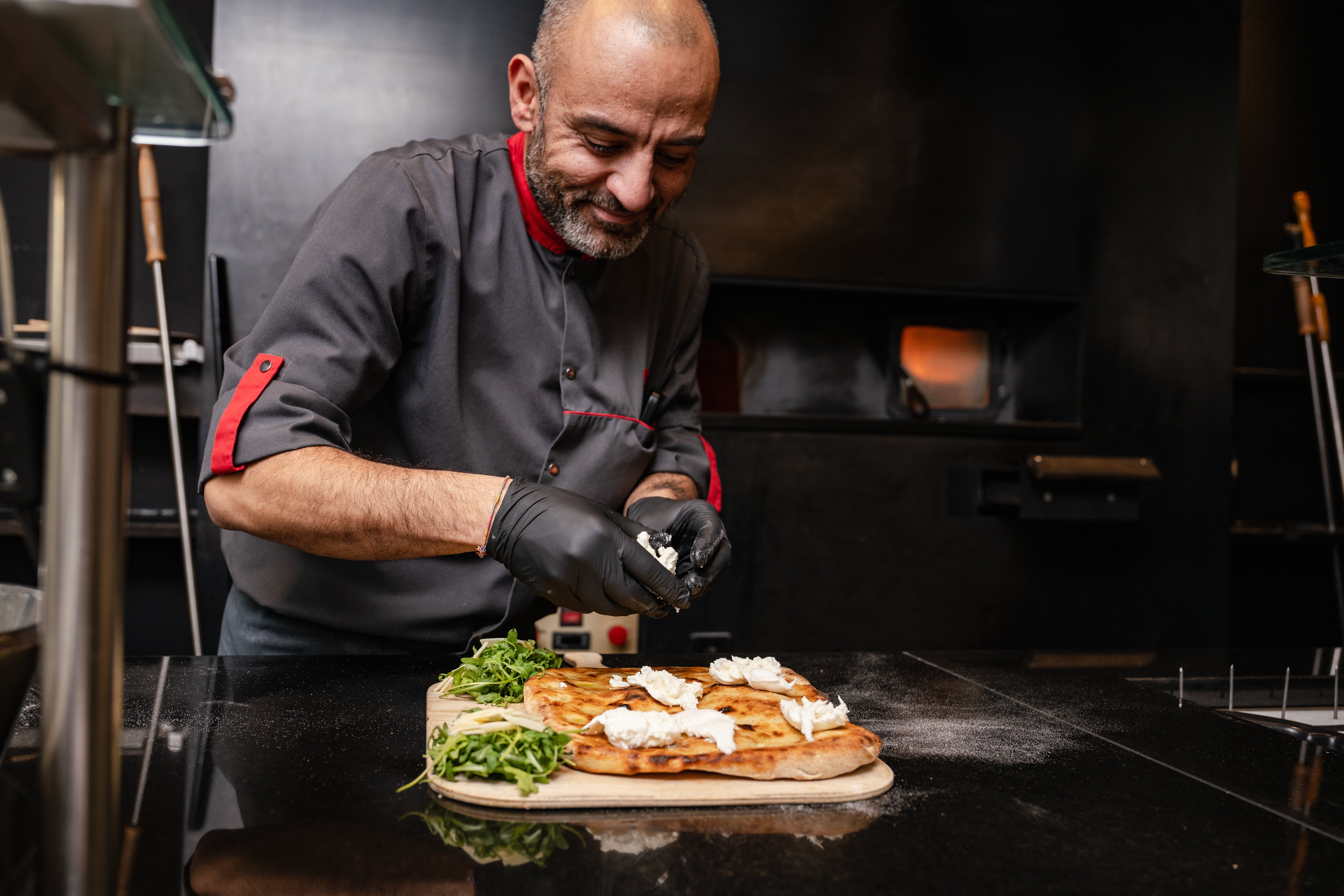 A professional chef preparing a pizza in a clean, dark kitchen, in Laax, Switzerland.