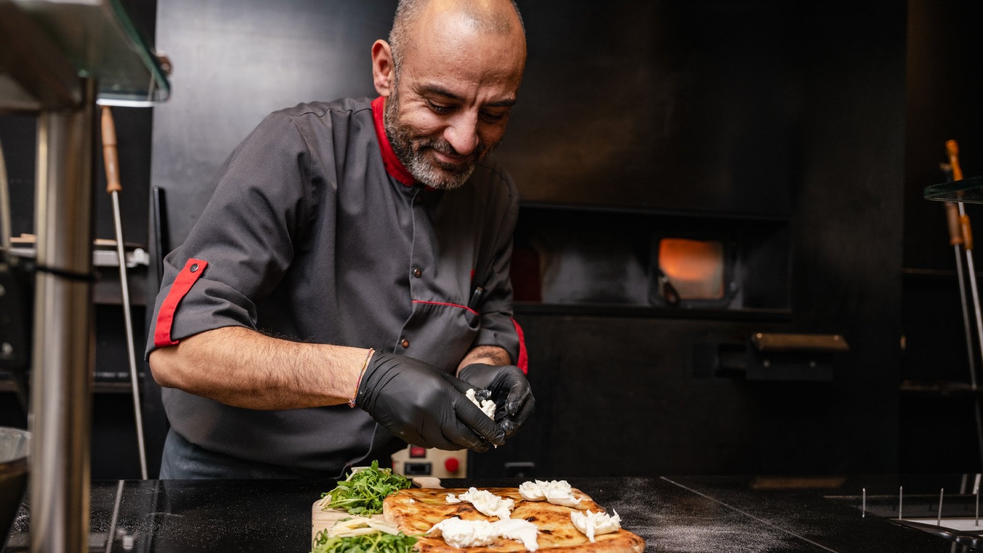 A professional chef preparing a pizza in a clean, dark kitchen, in Laax, Switzerland.