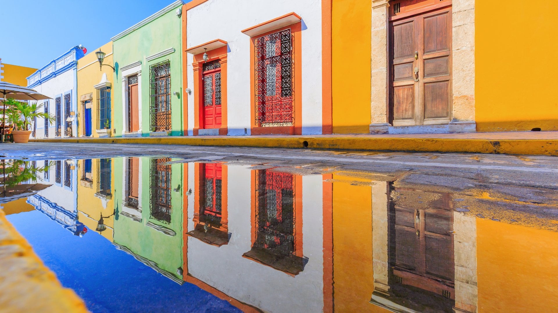 A line of bright, colourful cubic buildings in Campeche's old town, Mexico, reflected clearly in a puddle in the street