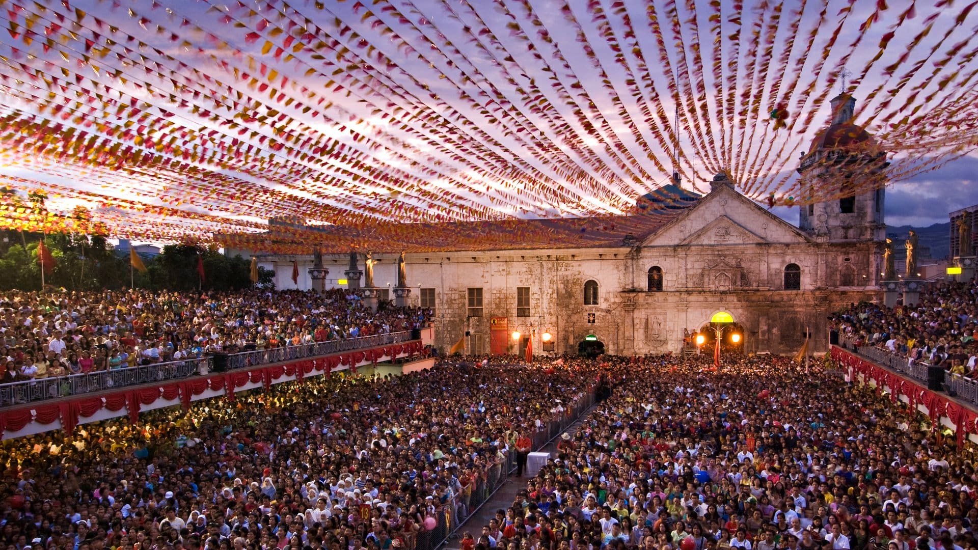A sunset celebration with a massive crowd in front of a building in Philippines.