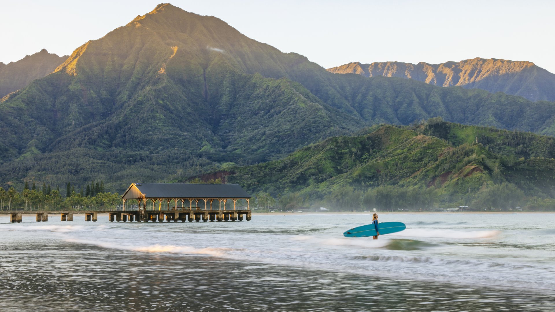 A woman is heading out for a surf in front of the pier at Hanalei Bay on the island of Kauai