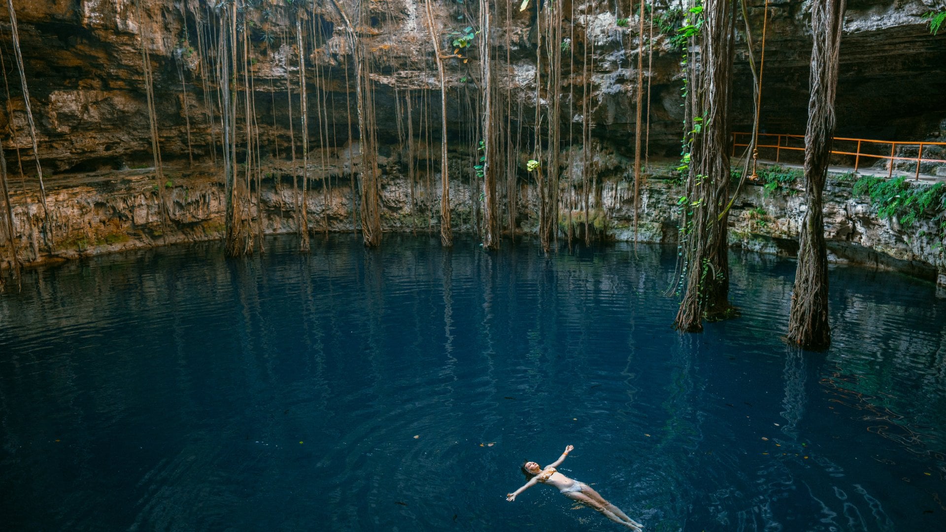 A woman swimming on her back in a deep blue cenote in Yucatan, Mexico.