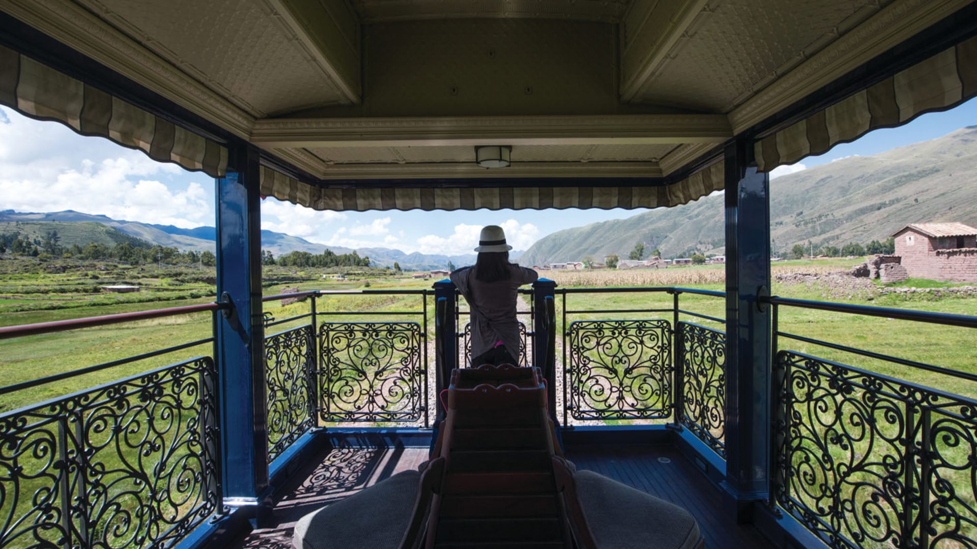 A woman in a hat stands on the observation deck of a train, the Andean Explorer, going through Peru from Cusco to Arequipa.