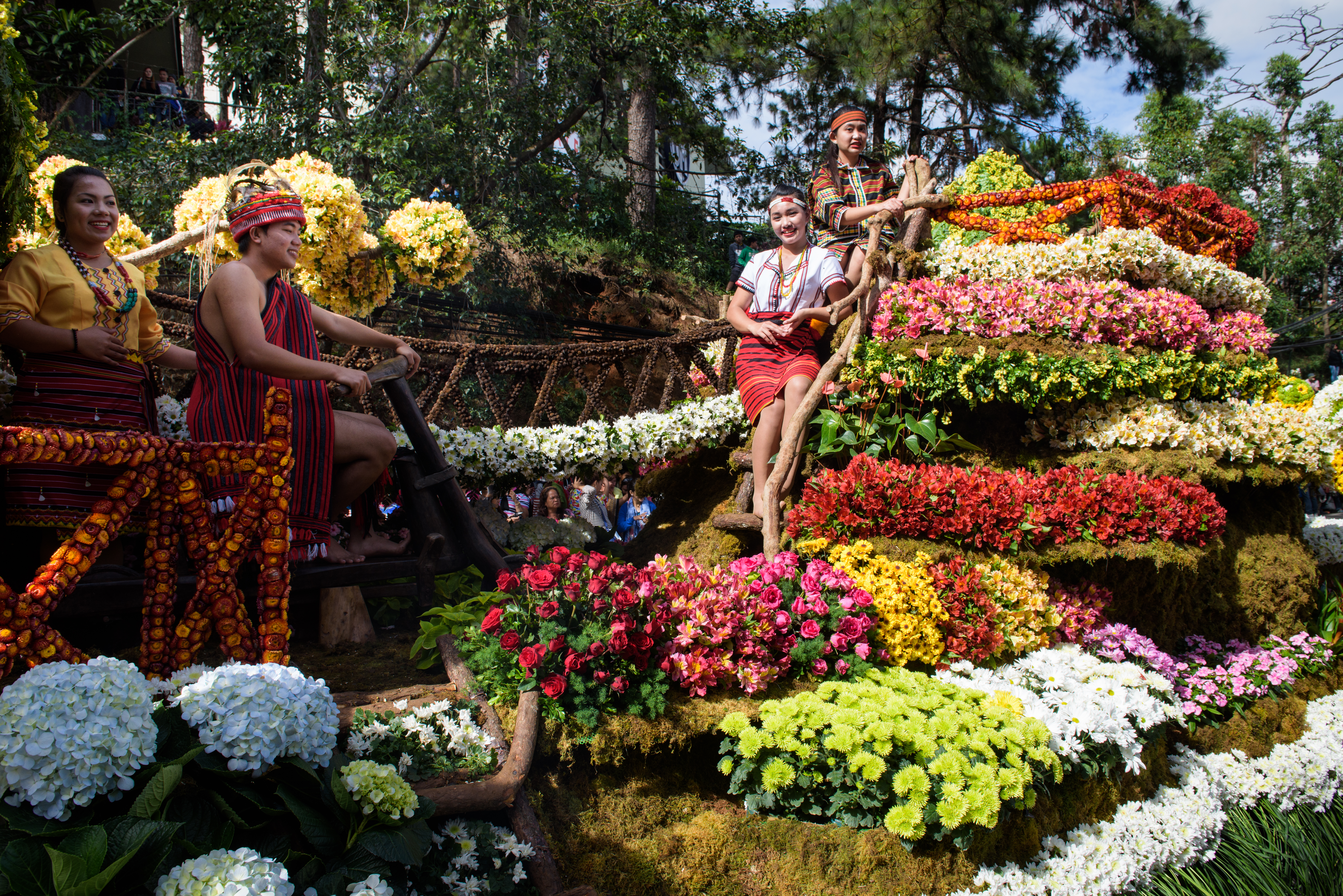 A group of people smiling in traditional Philippines atire, surrounded by colourful flowers in Baguio, Philippines.
