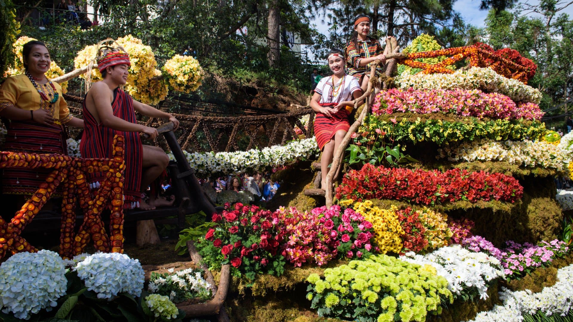 A group of people smiling in traditional Philippines atire, surrounded by colourful flowers in Baguio, Philippines.