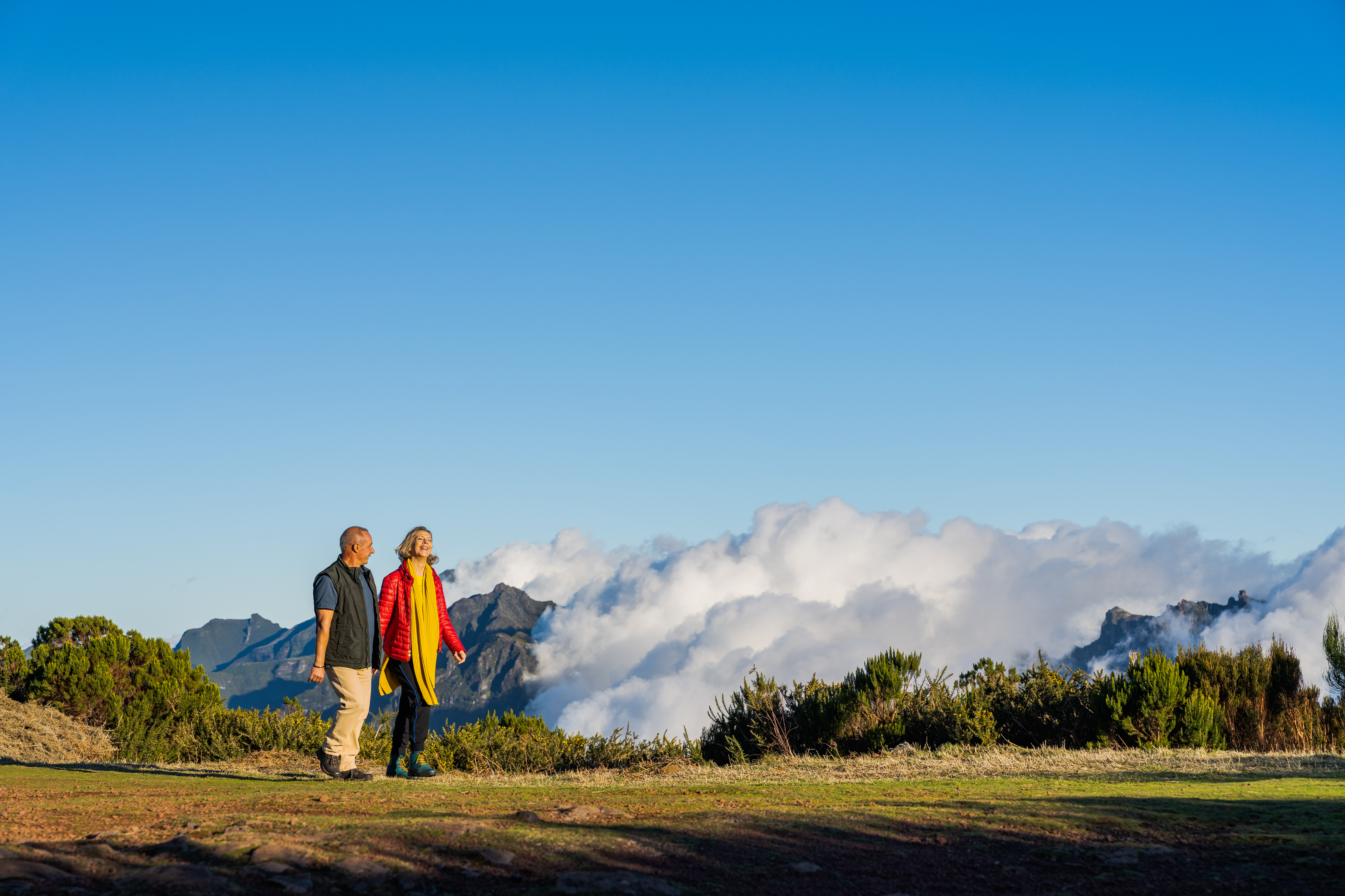 A man and woman walking outside in Madeira, Portugal, with clouds covering the mountains in the background.