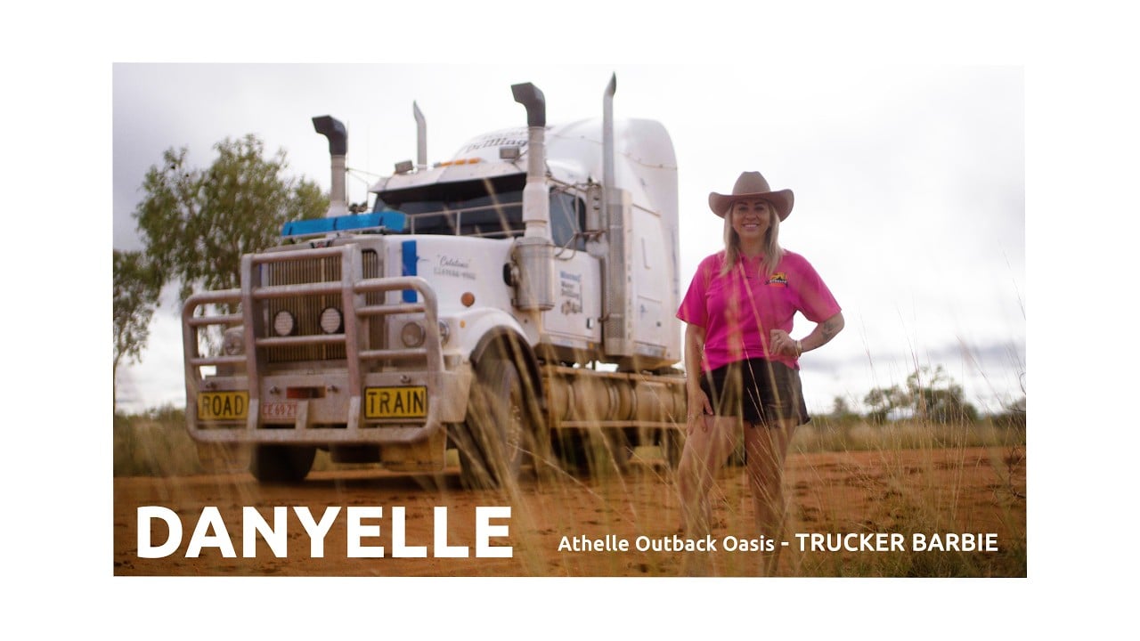 Danyelle of Athelle Outback Oasis smiling in a pink shirt and western hat in front of a triple axel truck in the outback of the Northern Territory, Australia.