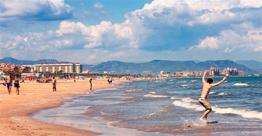 Beachgoers in Valencia, with a man boogyboarding in the foreground.