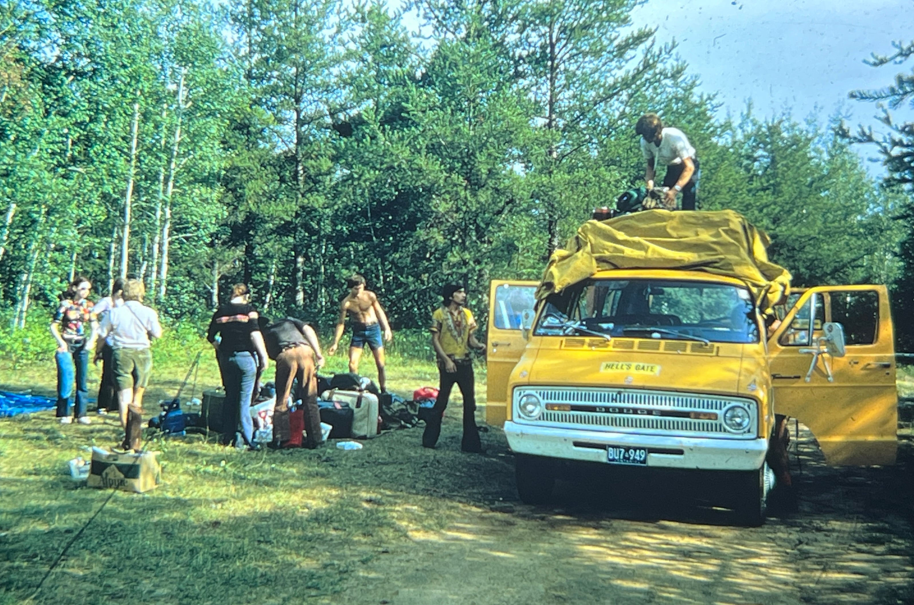 Vintage 1970s photo of a Goway camping tour group unloading luggage from a yellow Dodge minibus at a forest campsite