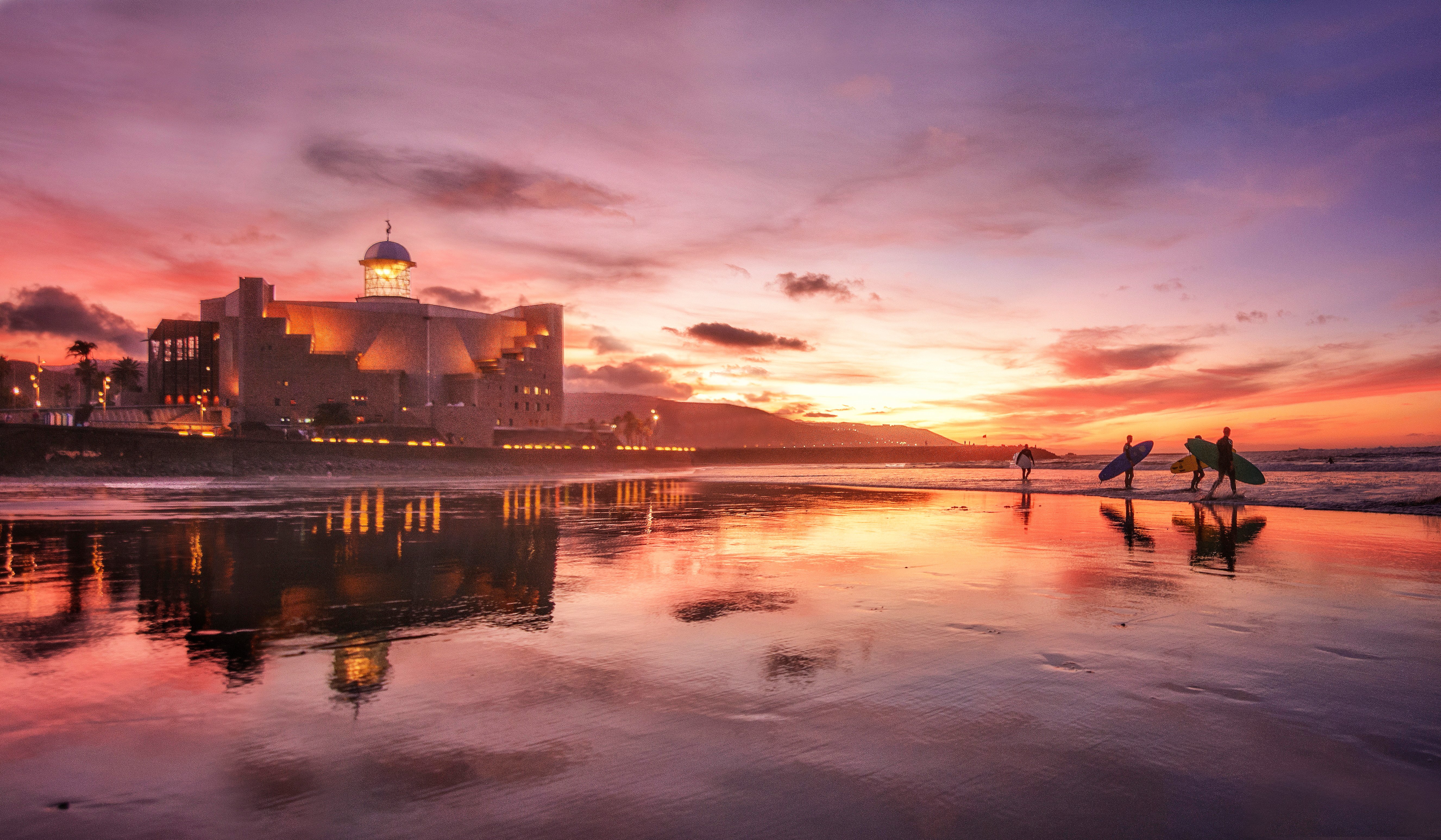 A group of surfers walking along a beach in Las Palmas, Gran Canaria, at sunset.