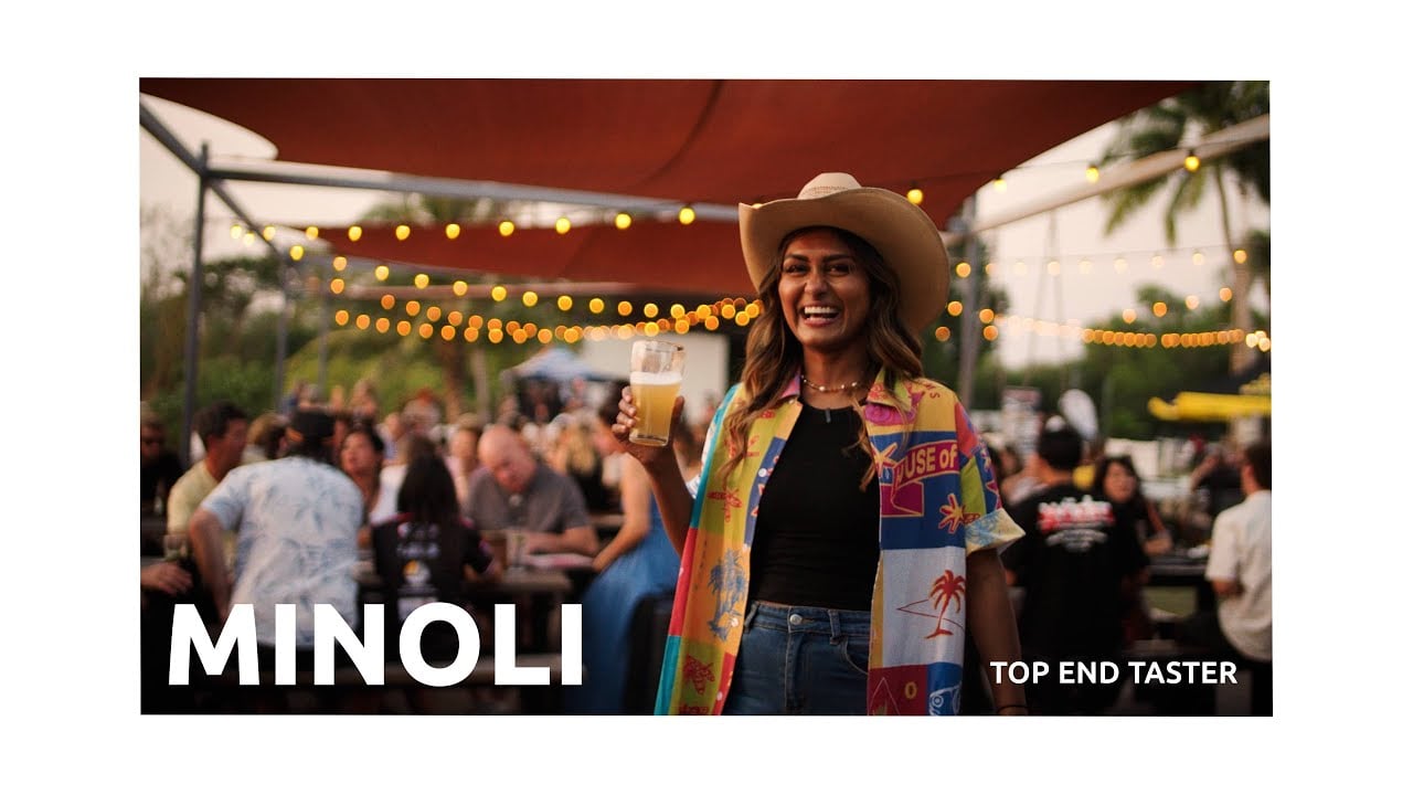 Minoli of Ella by Minoli smilling in a colourful patterned shirt with a beer in her hand at an outdoor beer market in Darwin, Northern Territory, Australia.