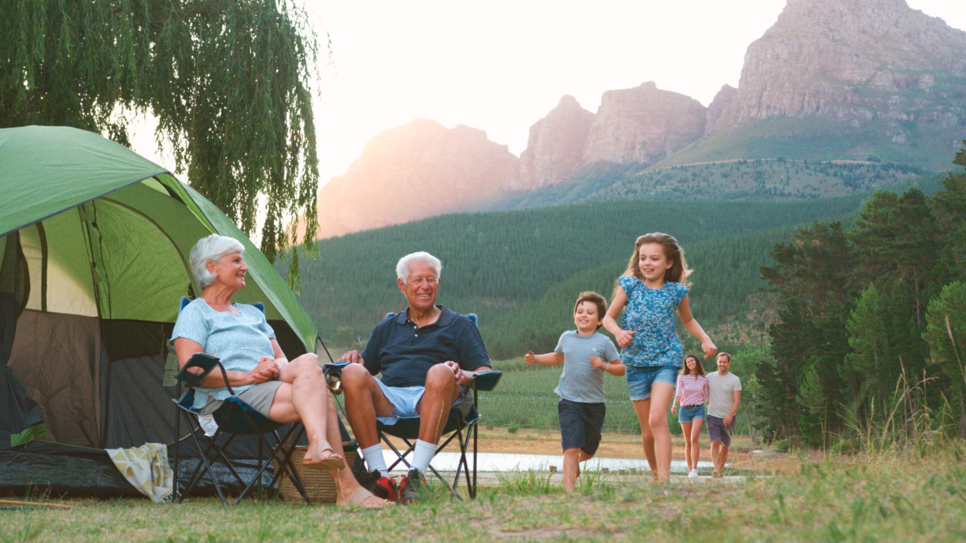 Multi Generation Family On Camping Trip In Countryside By Lake Relaxing As Children Play