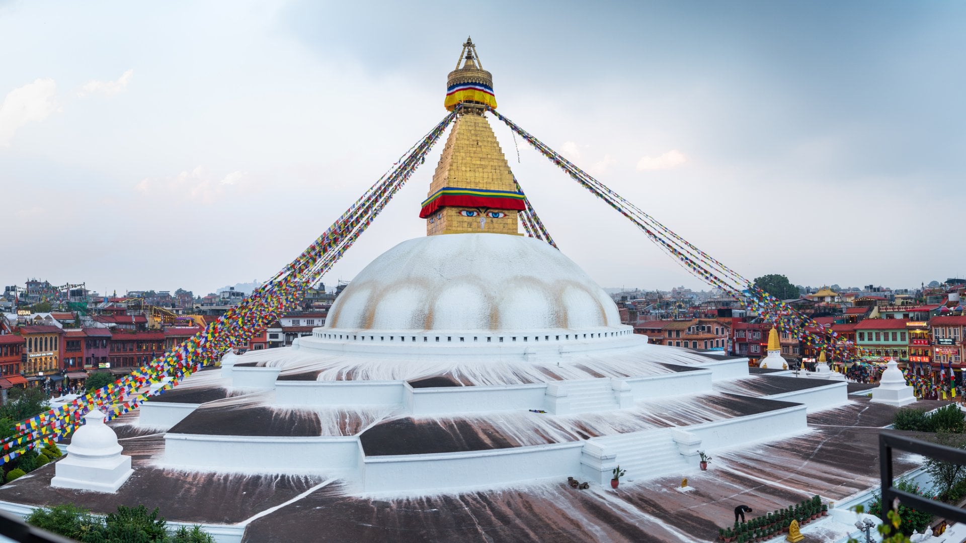 Multicolored praying flags hinged on Boudhanath Stupa - the largest spherical stupas in Nepal and sacred place for Buddhists. Panorama shot with walking pilgrims.