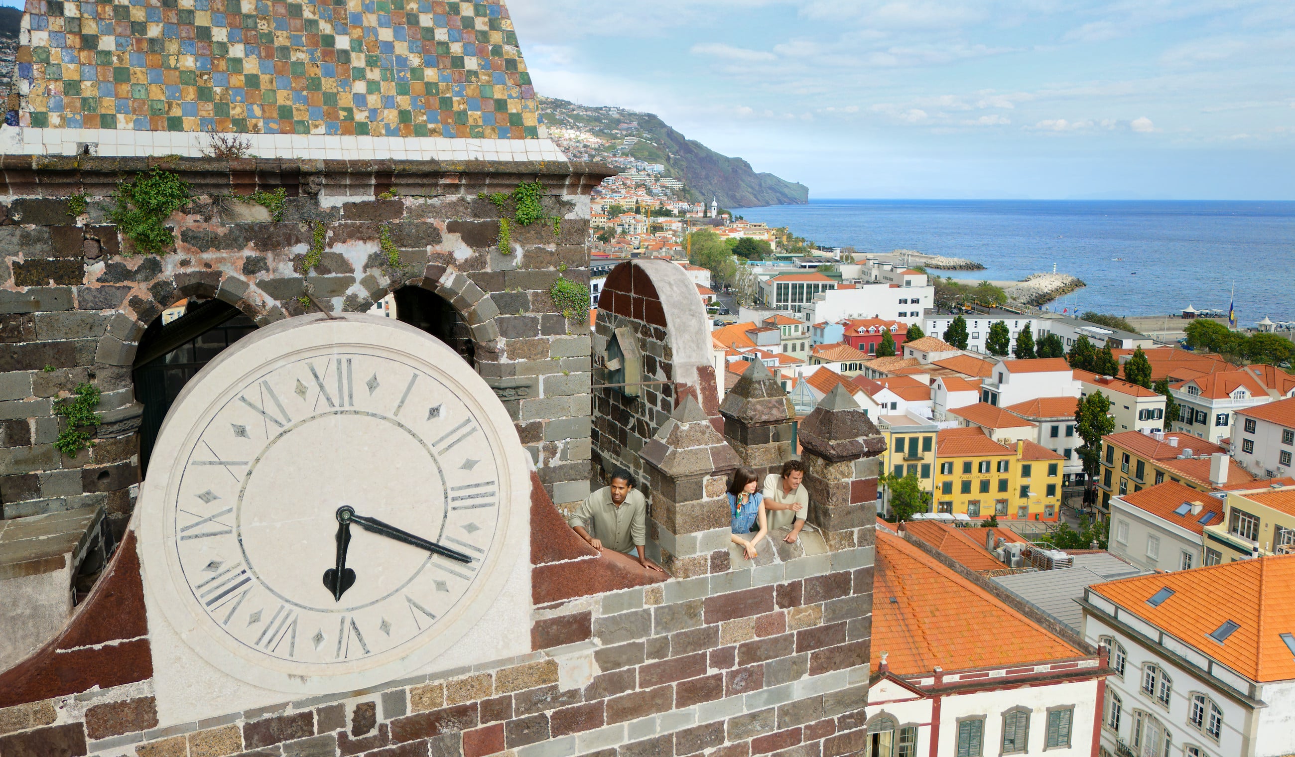 Three people overlooking Funchal, Madeira, Portugal, from the top of a clock tower.