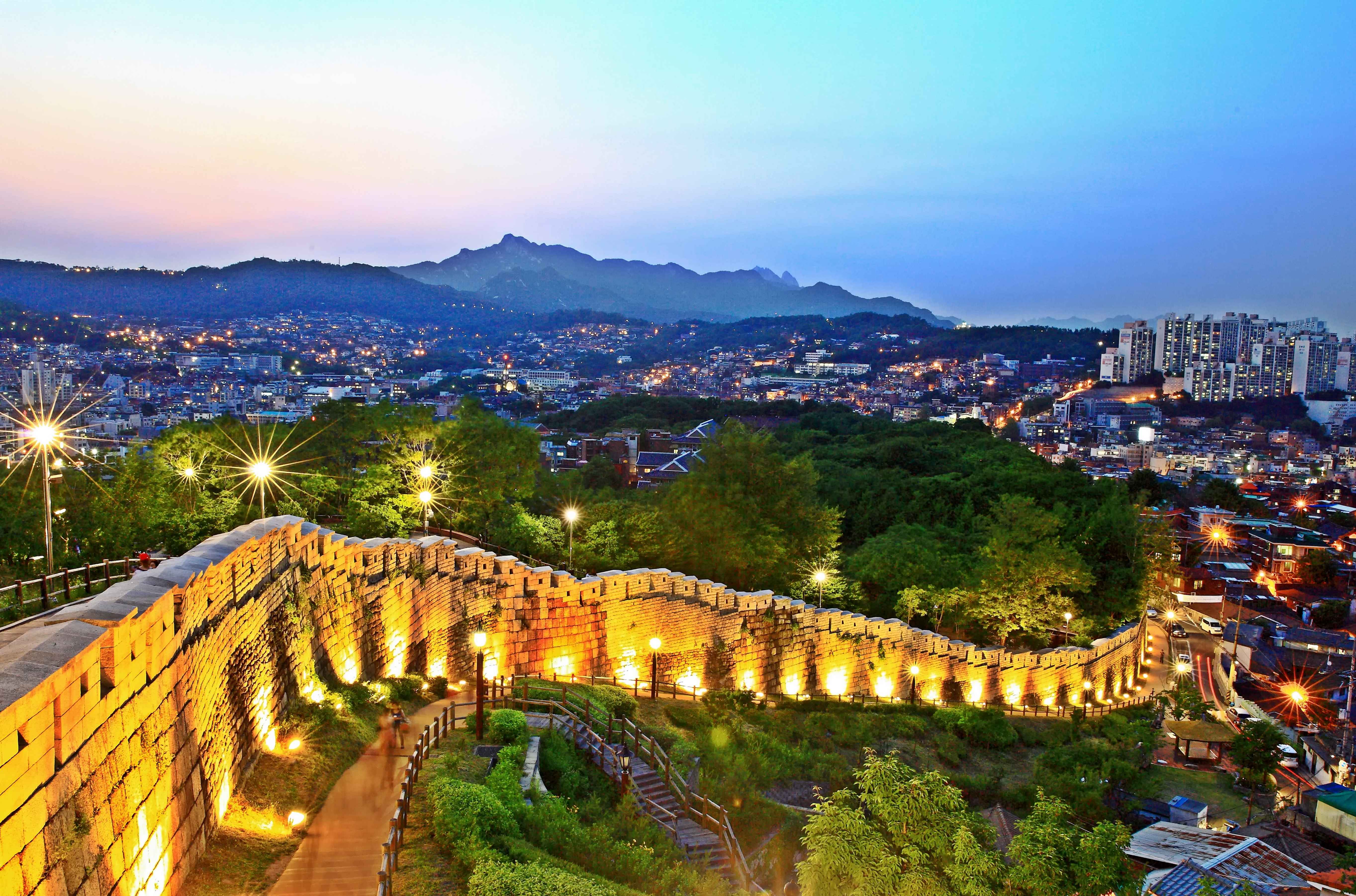 View of Seoul City Wall with the city's urban area in the background, at sunset.