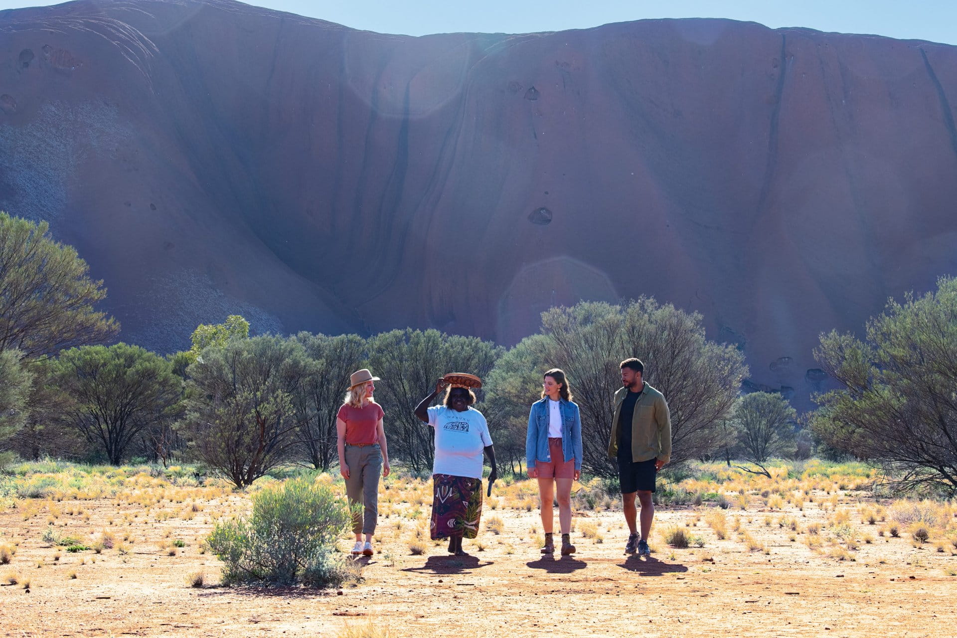 A ground level shot of an Aboriginal Australian woman leading a group of three people, two women and one man, on a tour in front of Uluru, formerly Ayers Rock.