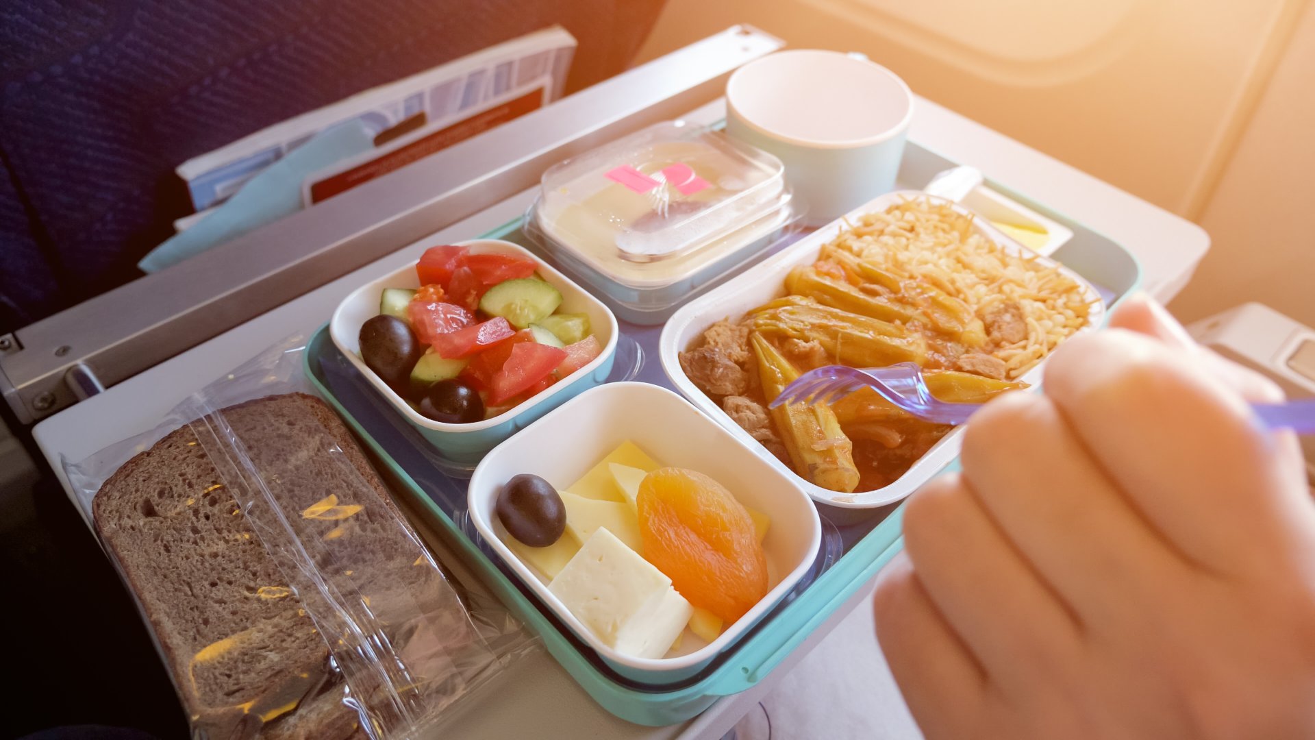 Woman eats in airplane during flight food served on a tray, hand closeup