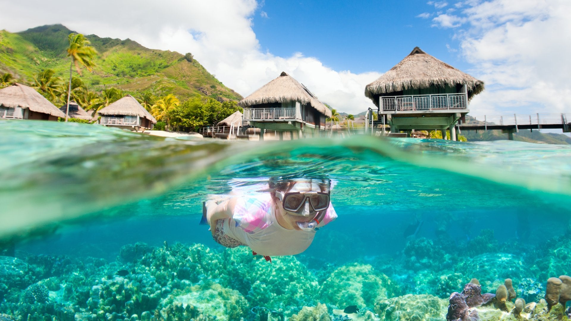 Woman snorkeling in clear tropical waters in front of overwater bungalows