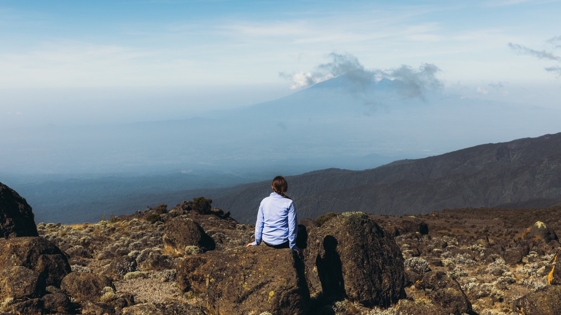 Woman traveler relaxing after the hiking trip feeling success enjoying the view of the Meru mountain from the Mount Kilimanjaro, Tanzania