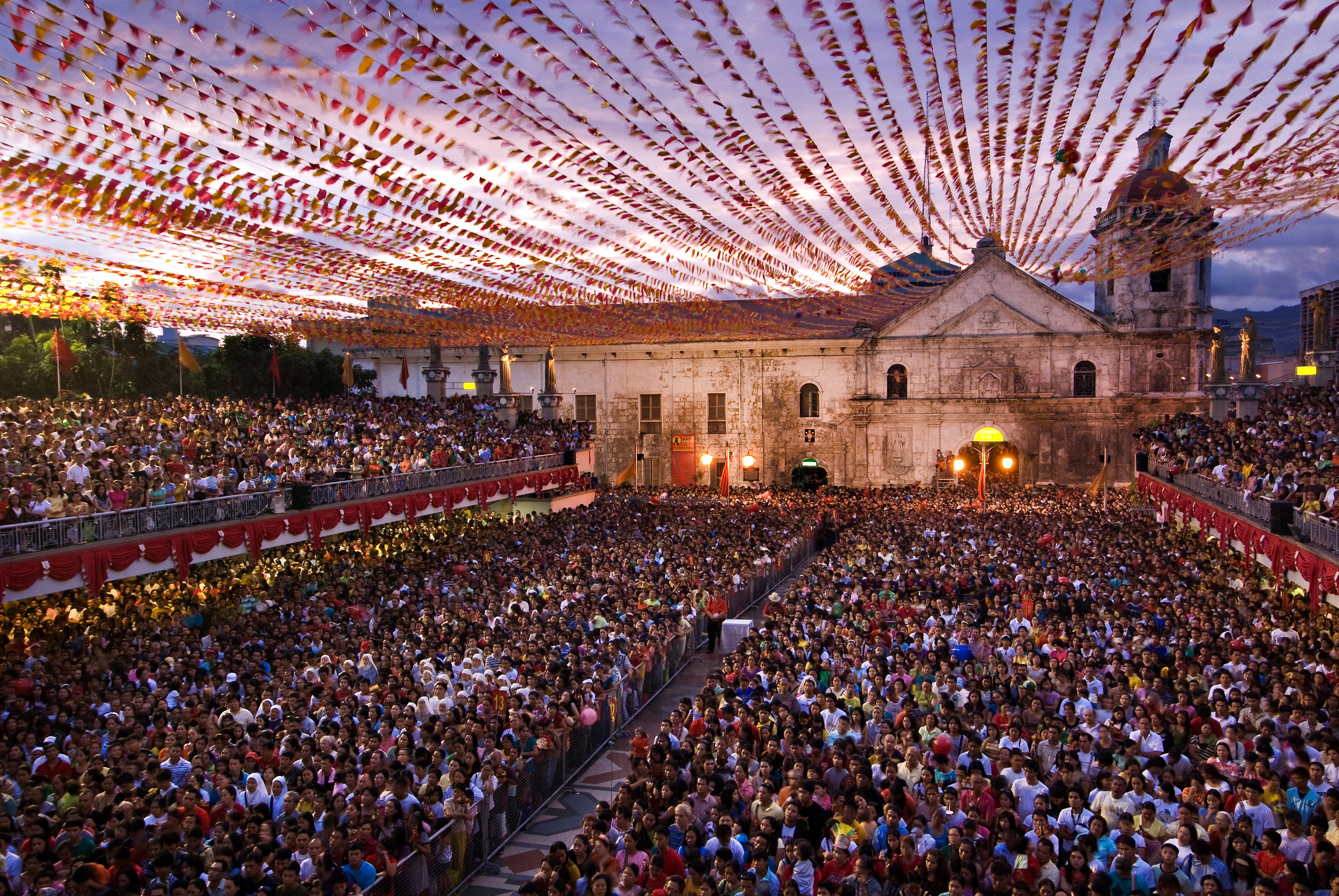 A sunset celebration with a massive crowd in front of a building in Philippines.