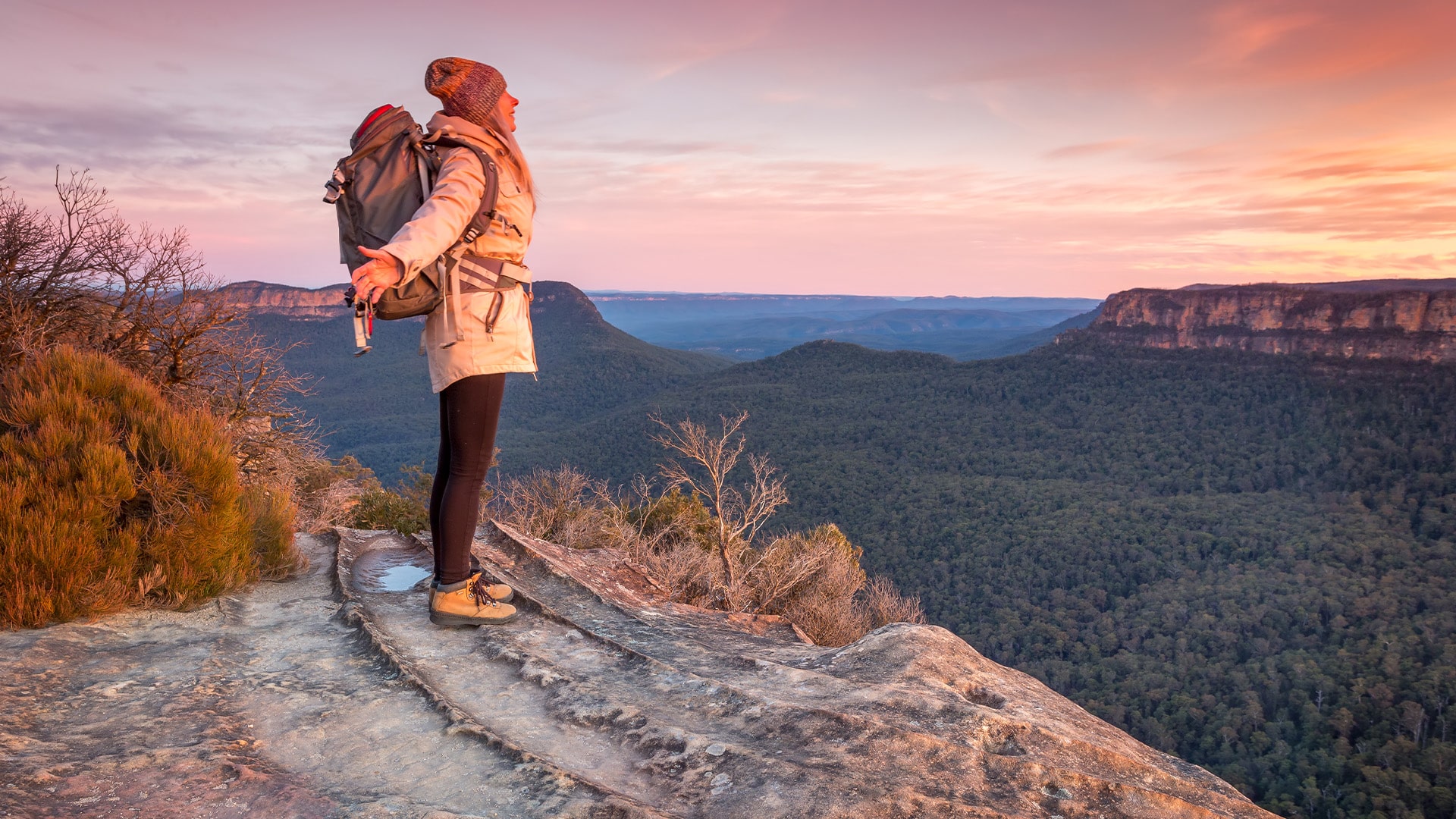 woman standing on edge of mountains with red sunset