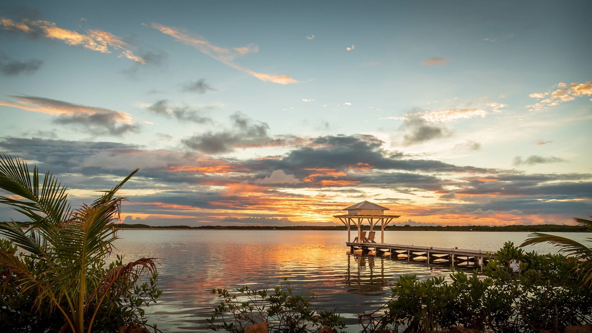 Two people siting on the end of a dock in Ambergris Caye at sunset