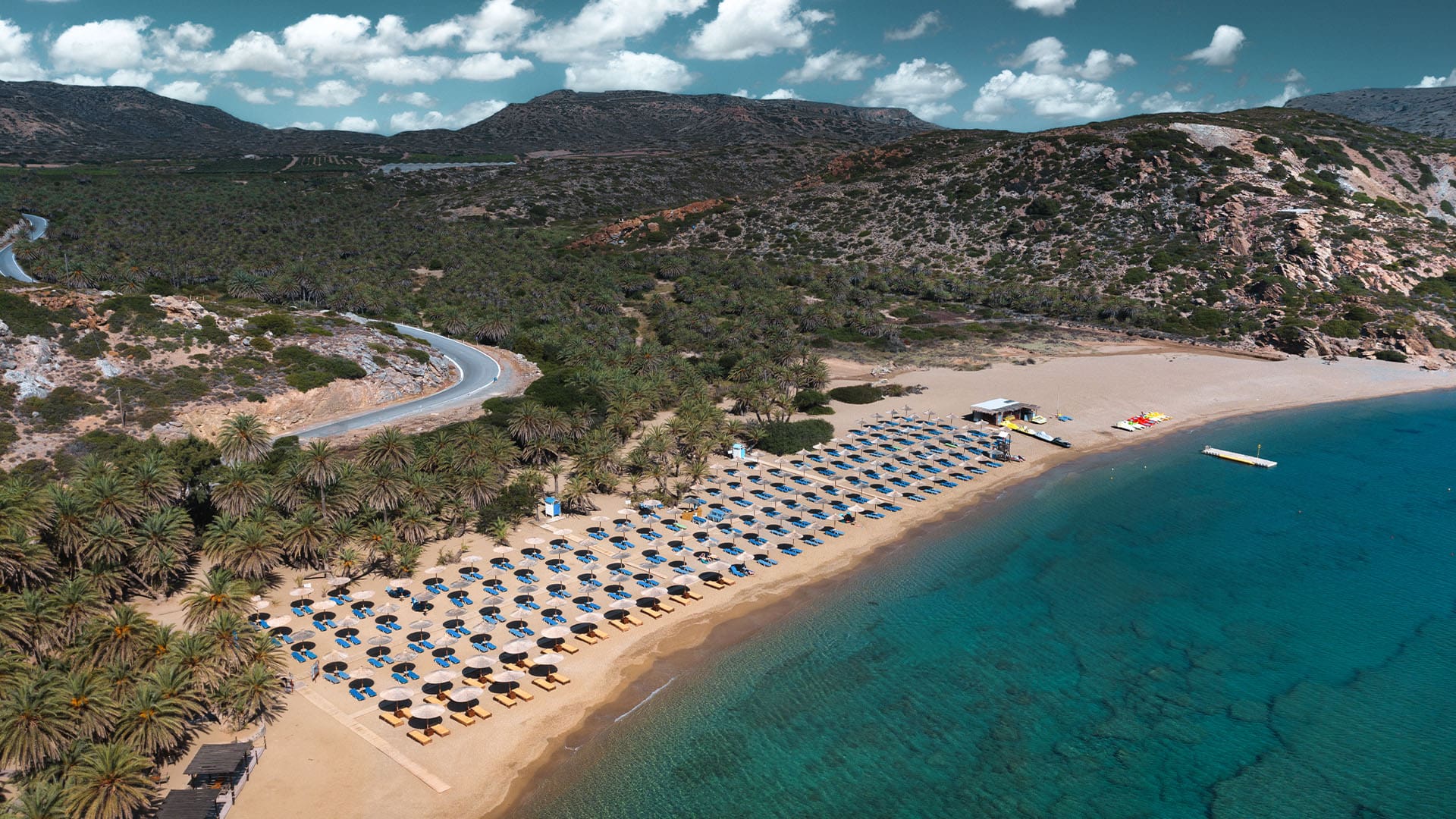 aerial view of umbrellas and lounging chairs along a pristine stretch of beach on the Greek island of Crete