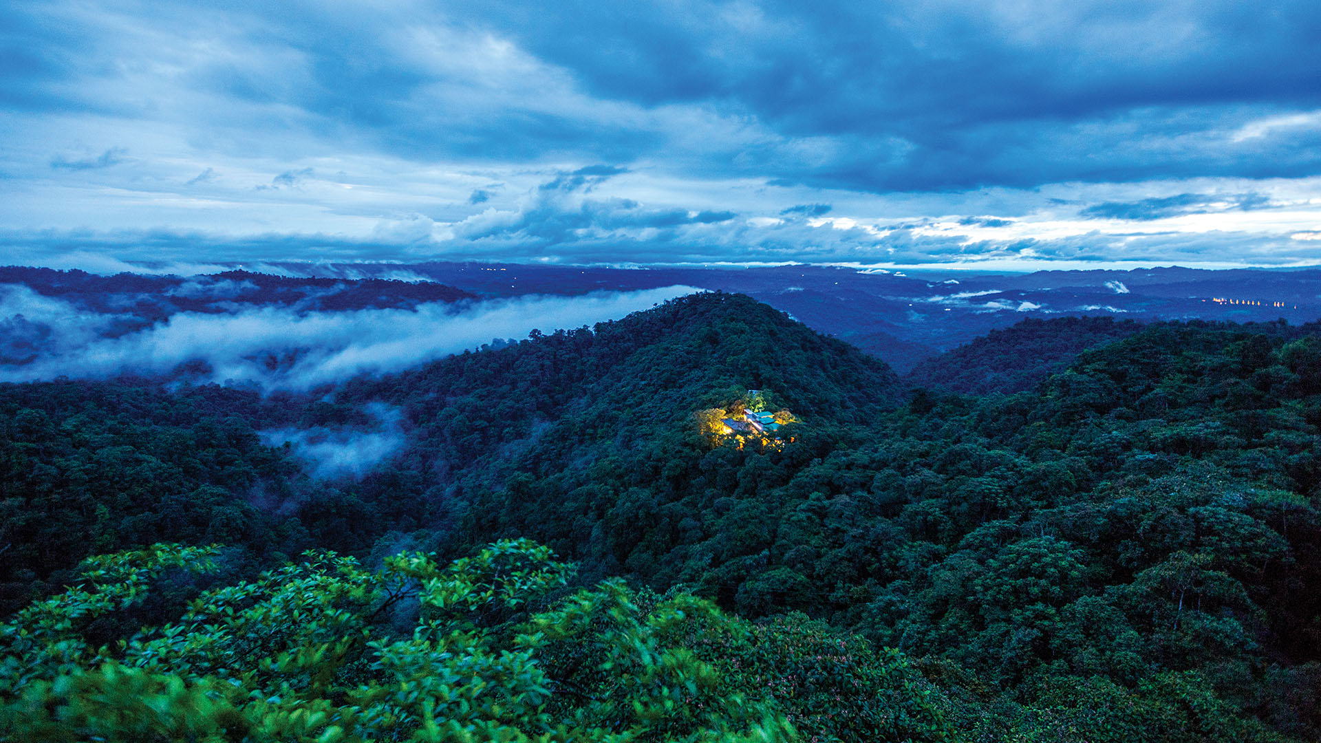 An aerial view of Mashpi Loge at dusk, nestled in the lush, cloud covered hills outside Quito