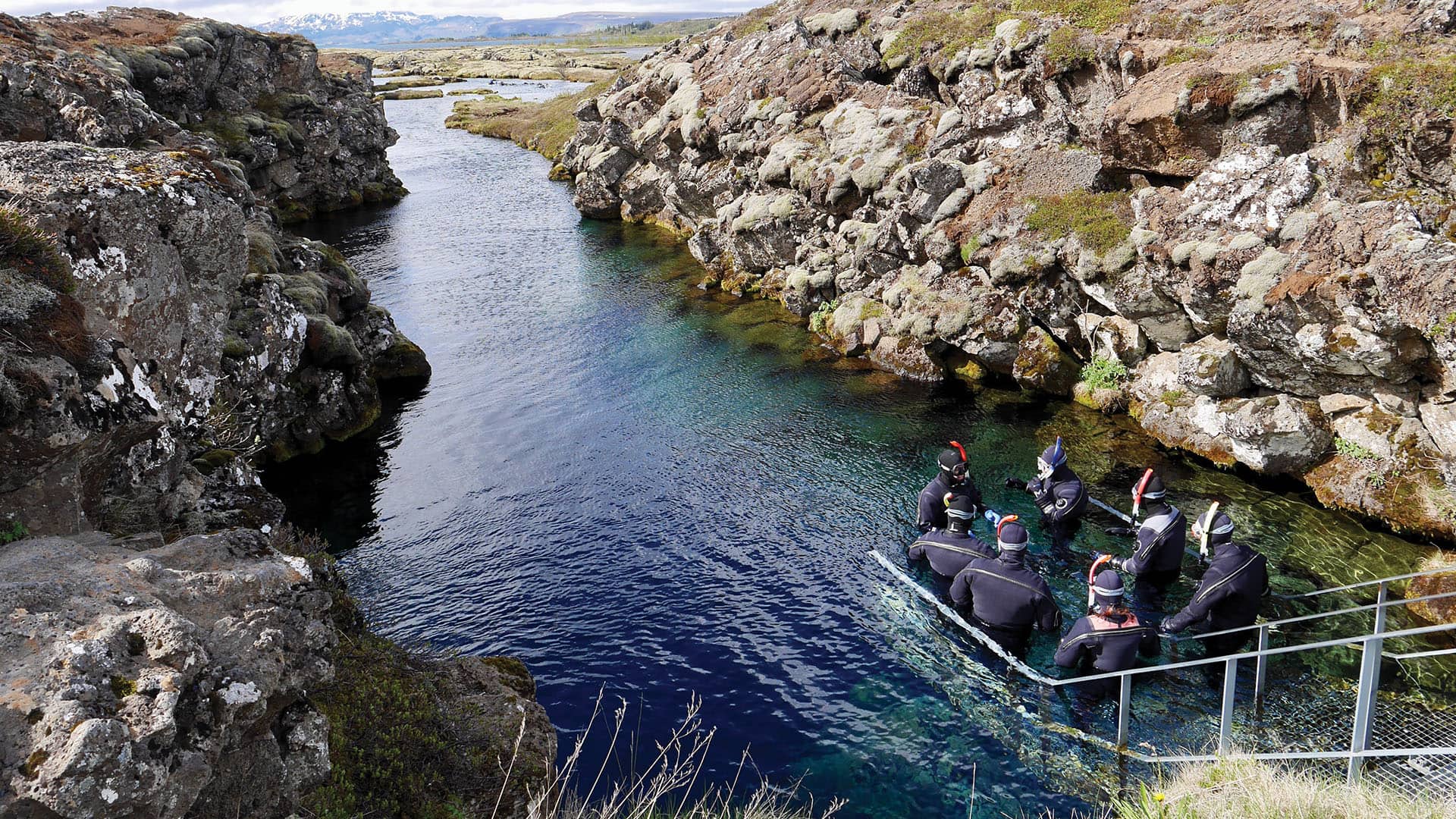 A group of snorkelers walking into the clear waters of the Silfra Fissure