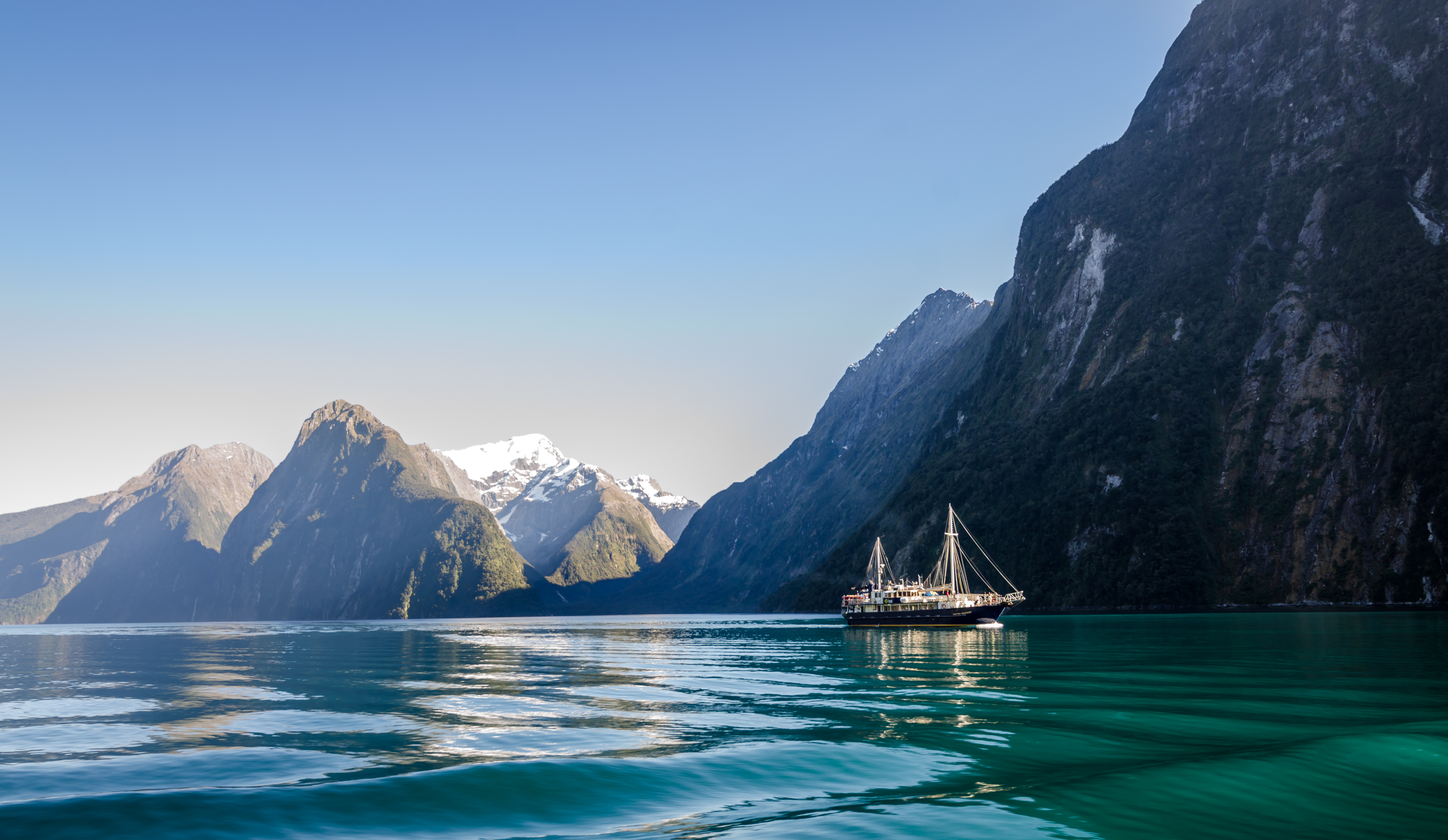 A sailboat floating through Milford Sound in New Zealand during a misty morning.