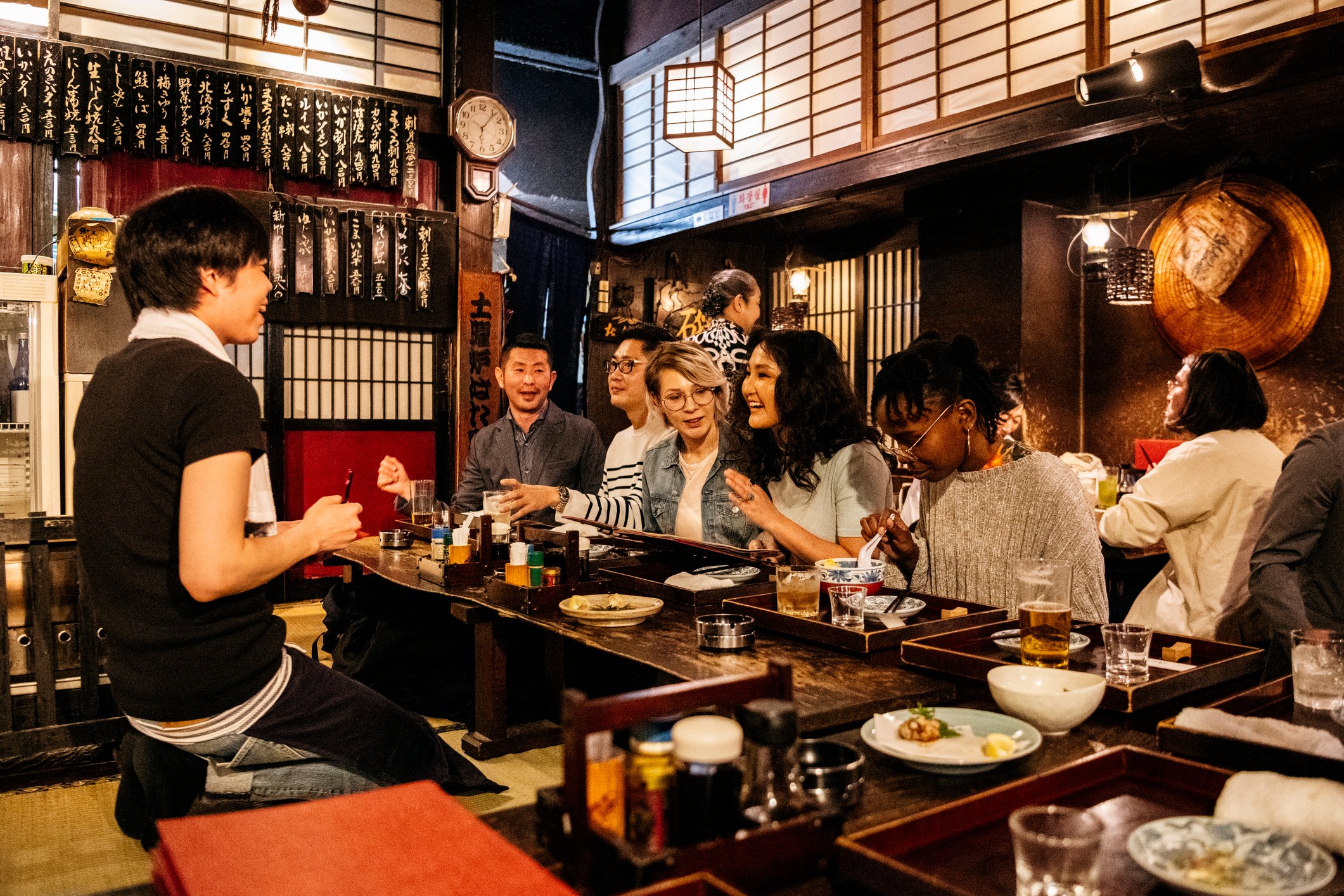 Waiter taking food order from happy group of friends, night out, drinking, eating in Tokyo, Japan.