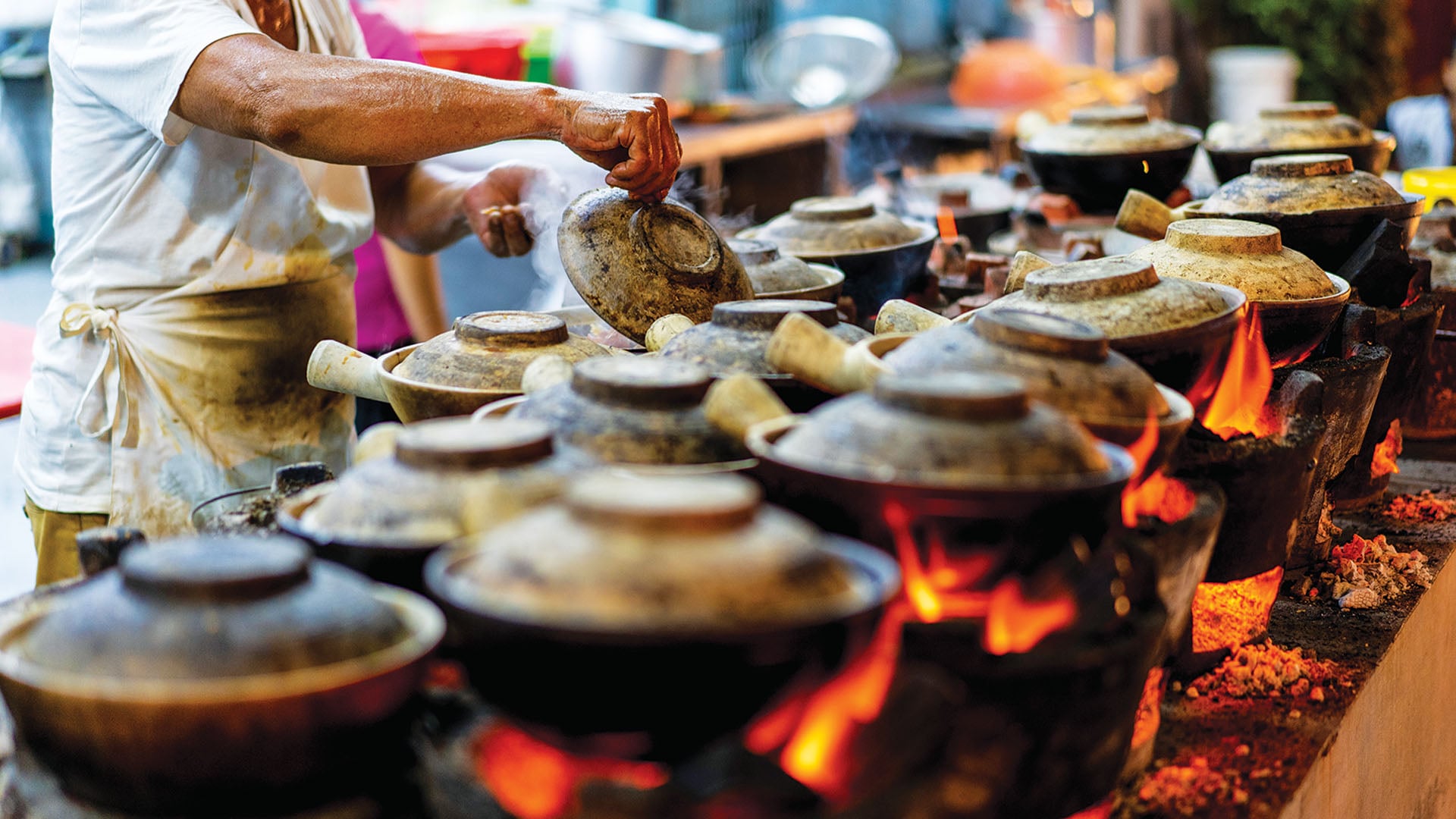 A hawker cooks in clay pots in the streets of Singapore.