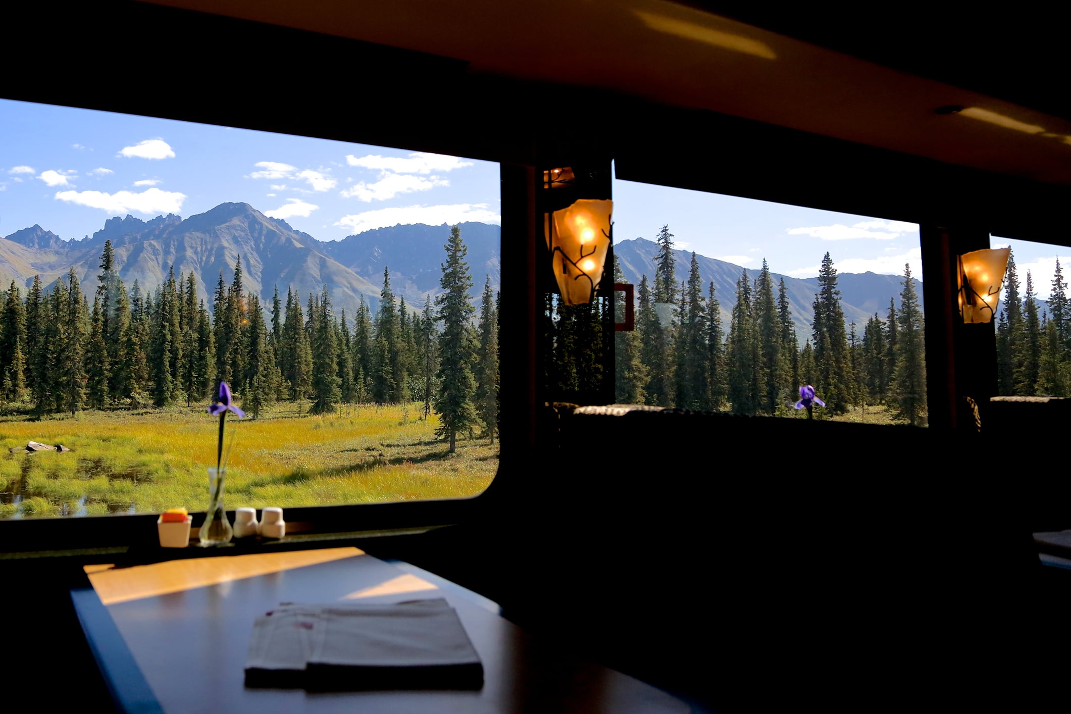 A sunny mountain range and forest outside a dining car on board a rail journey in Alaska, USA.