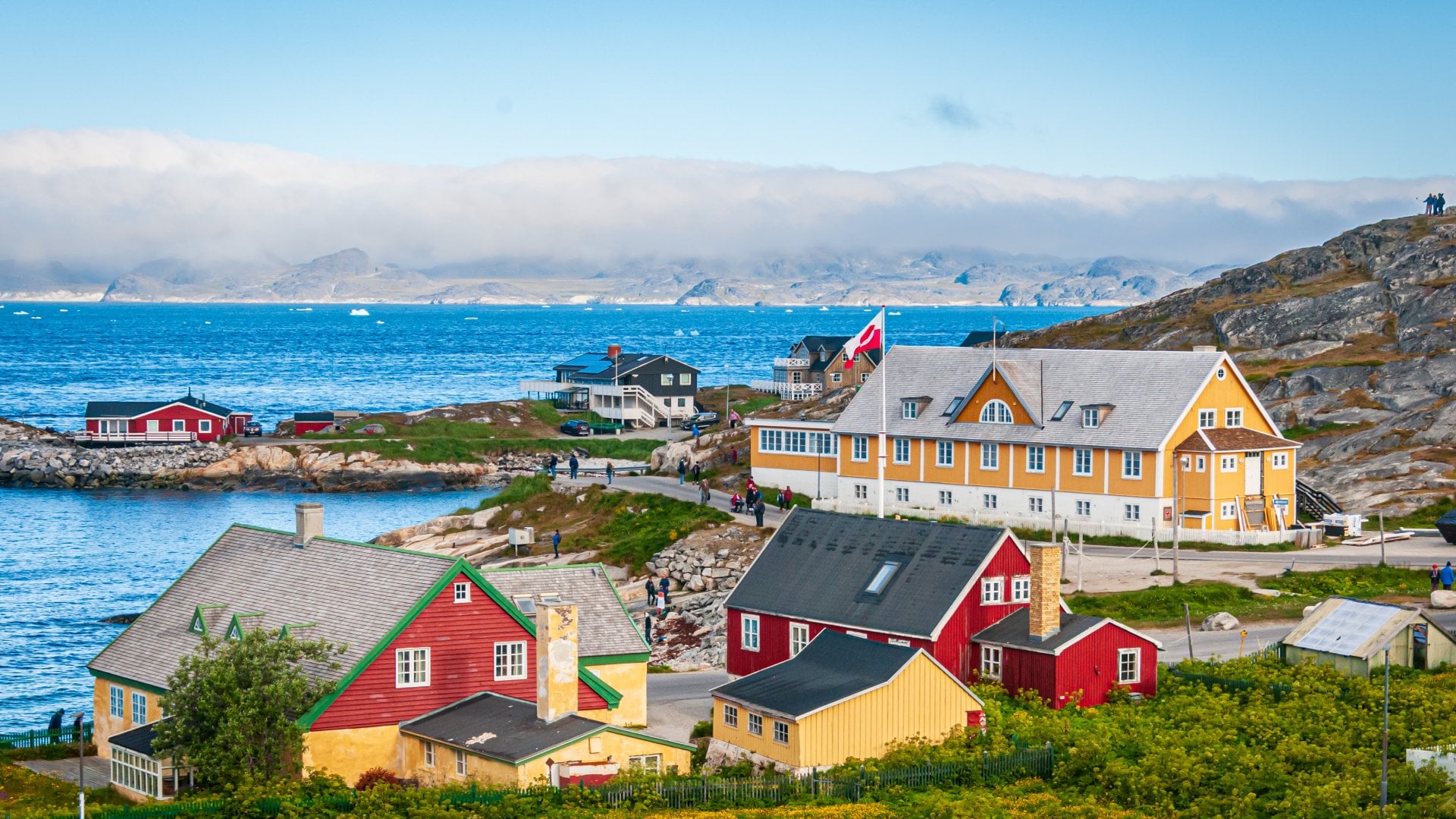 A fog bank covers the far shore and mountains as ice floes float past the colorful buildings and homes in Nuuk, Greenland