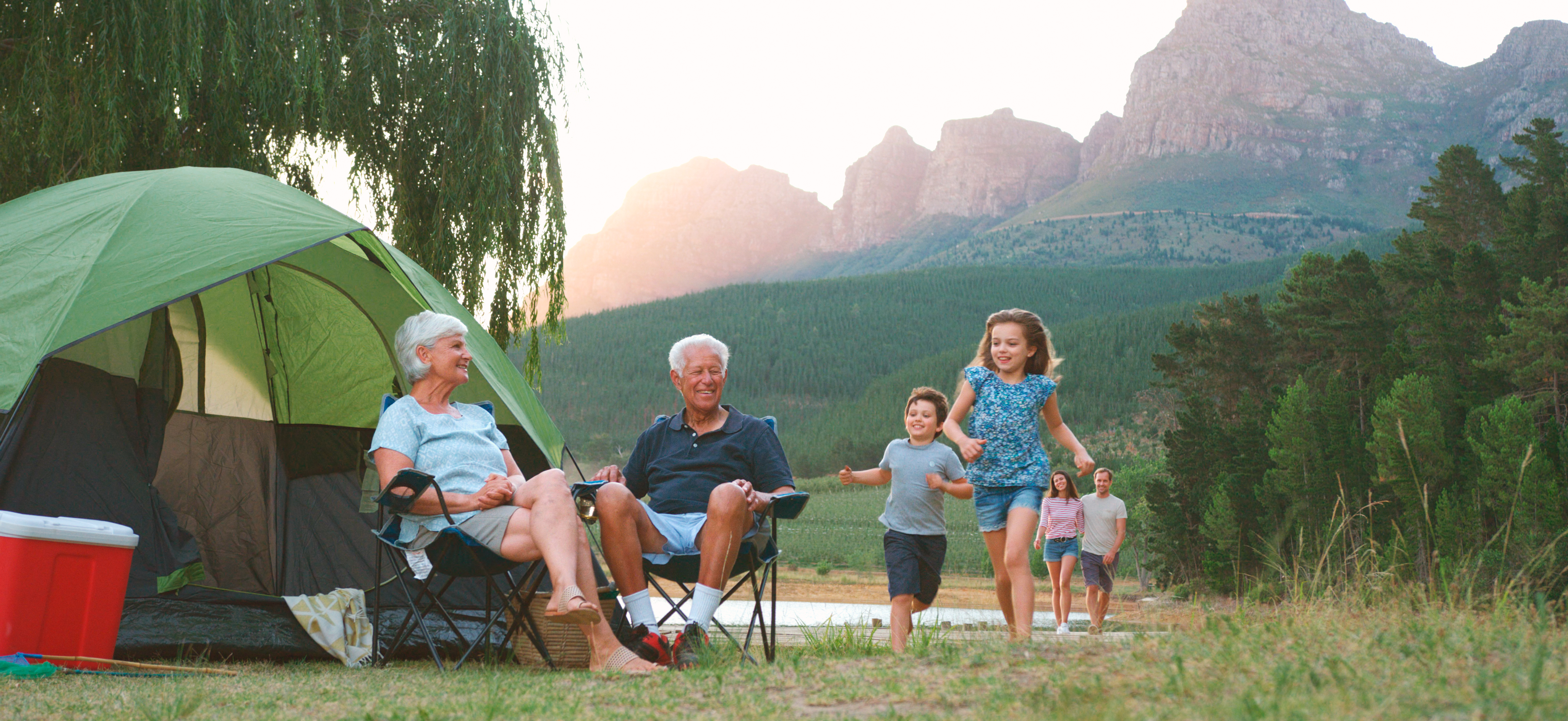 Multi Generation Family On Camping Trip In Countryside By Lake Relaxing As Children Play